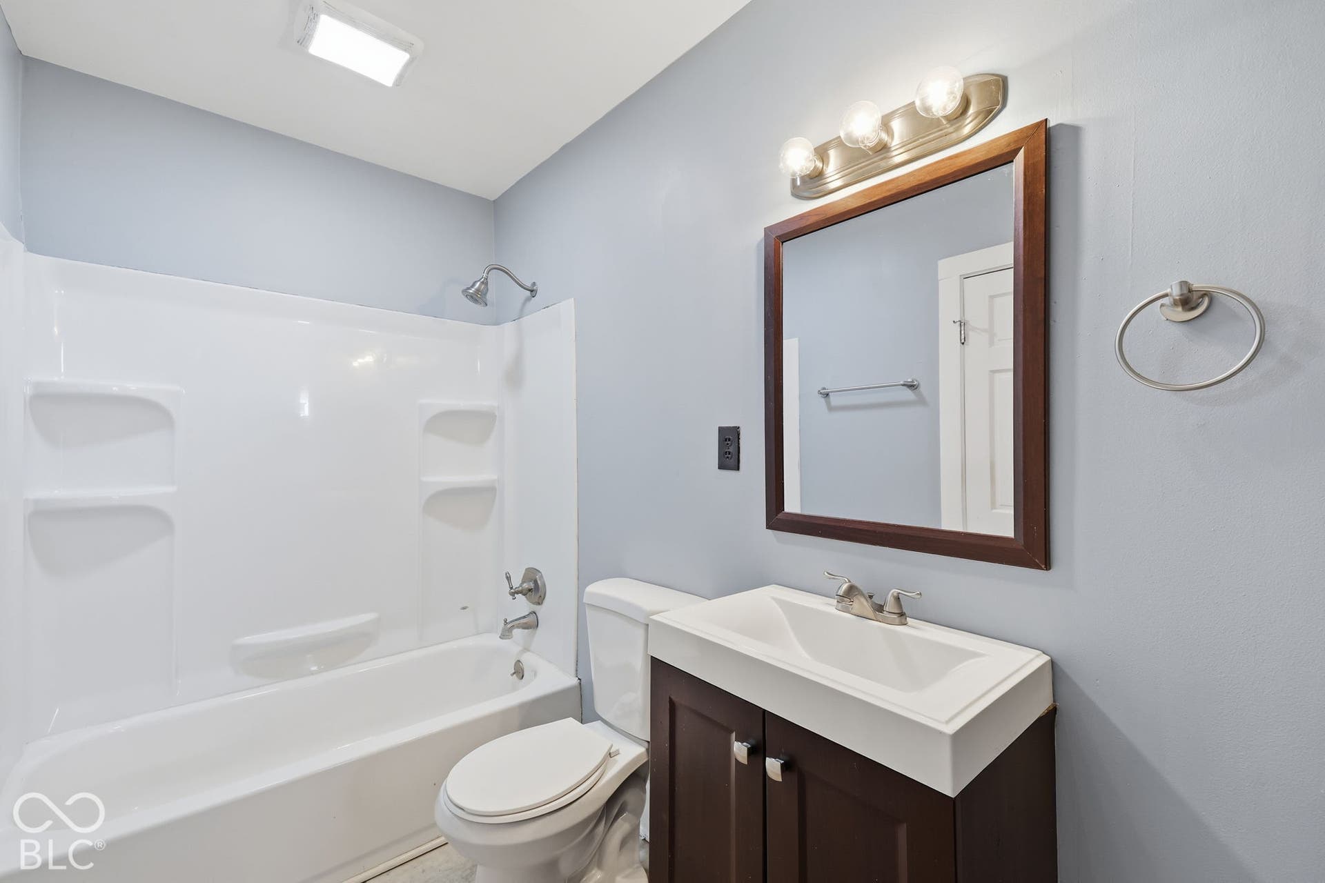 Integrated shower and tub unit, dark wood-finish vanity with a white countertop, framed mirror, and brushed nickel fixtures