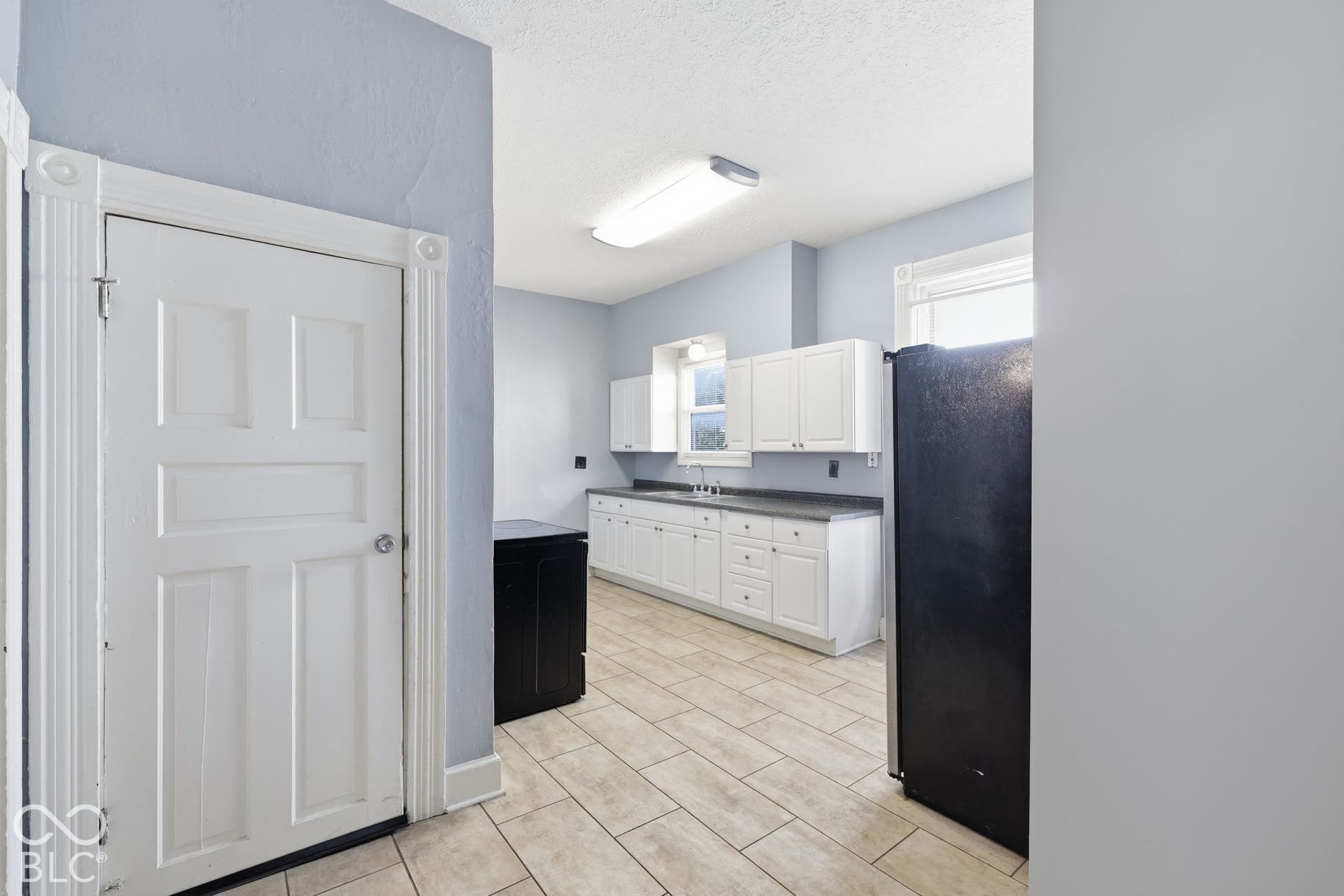 Kitchen featuring white cabinetry, dark countertops, a stainless steel sink, and light-toned tile flooring