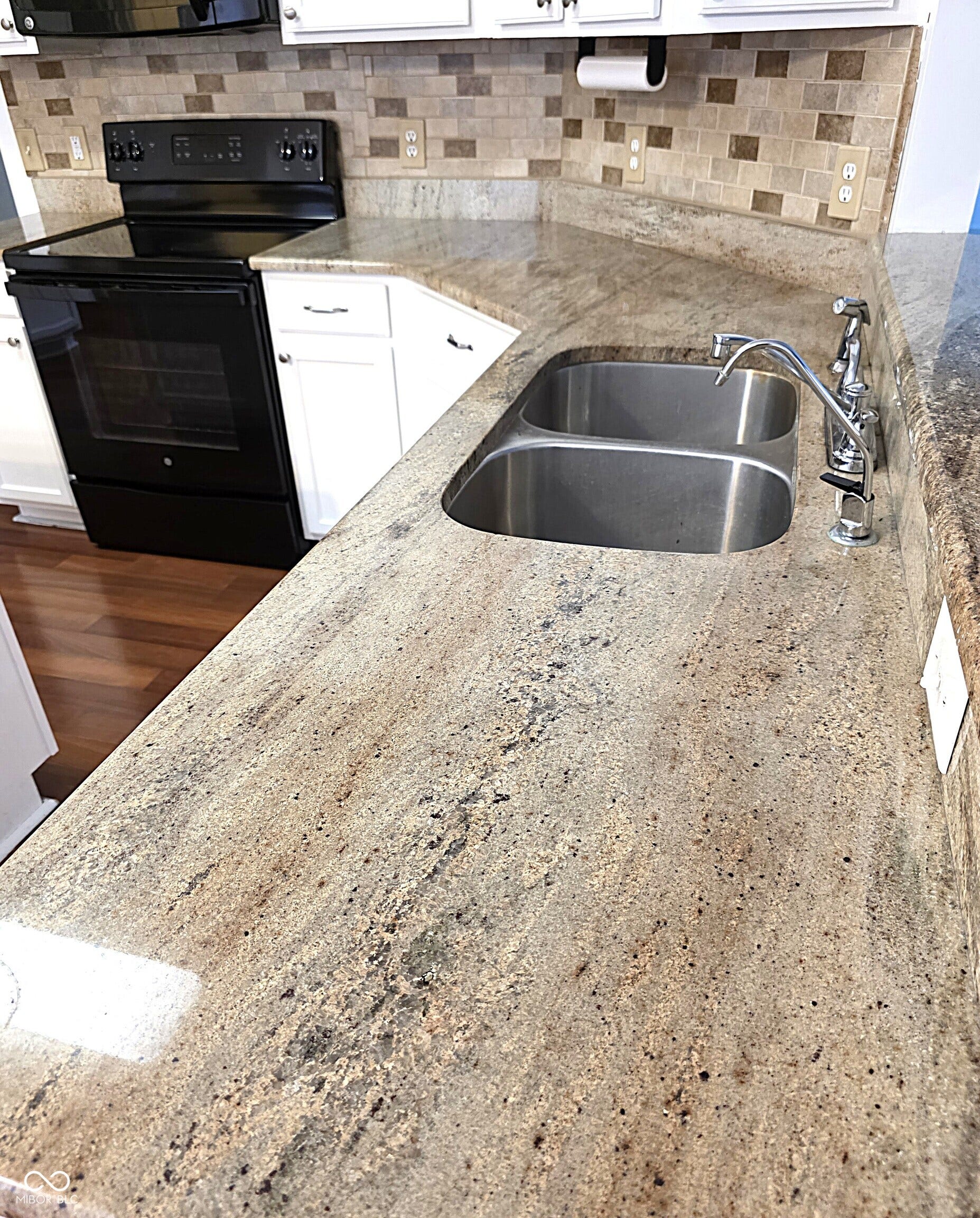 Expansive countertop space featuring a double basin stainless steel sink, tile backsplash, and white cabinetry