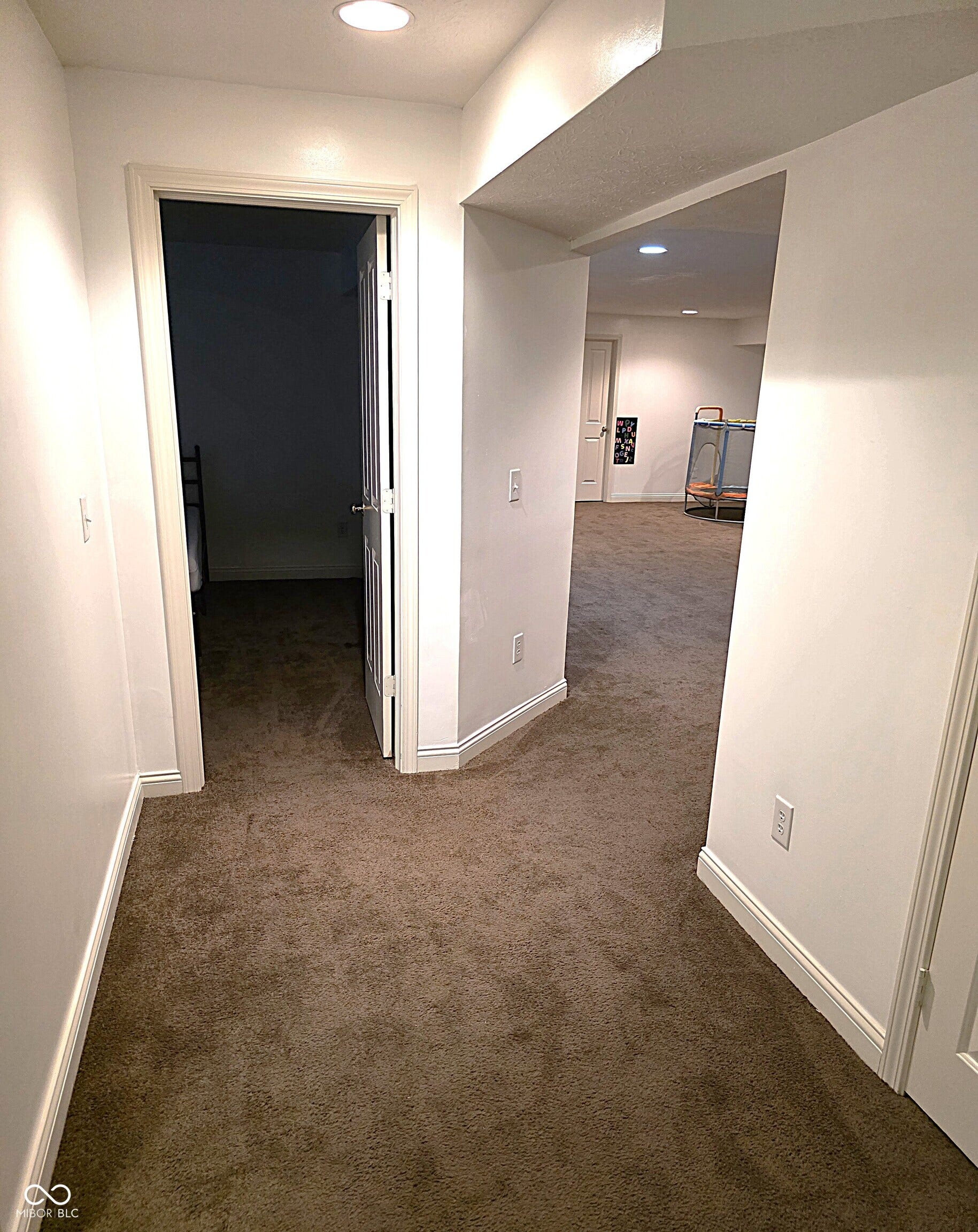 Recessed lighting illuminates the carpeted floor and crisp white wall finishes