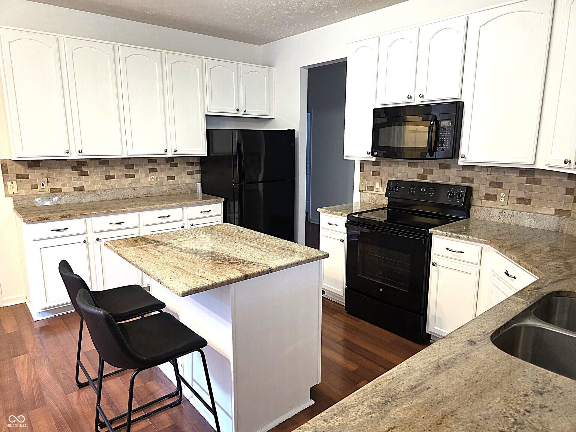 Kitchen featuring white cabinetry, granite countertops, a tiled backsplash, wood-finish flooring, and a stainless steel double basin sink