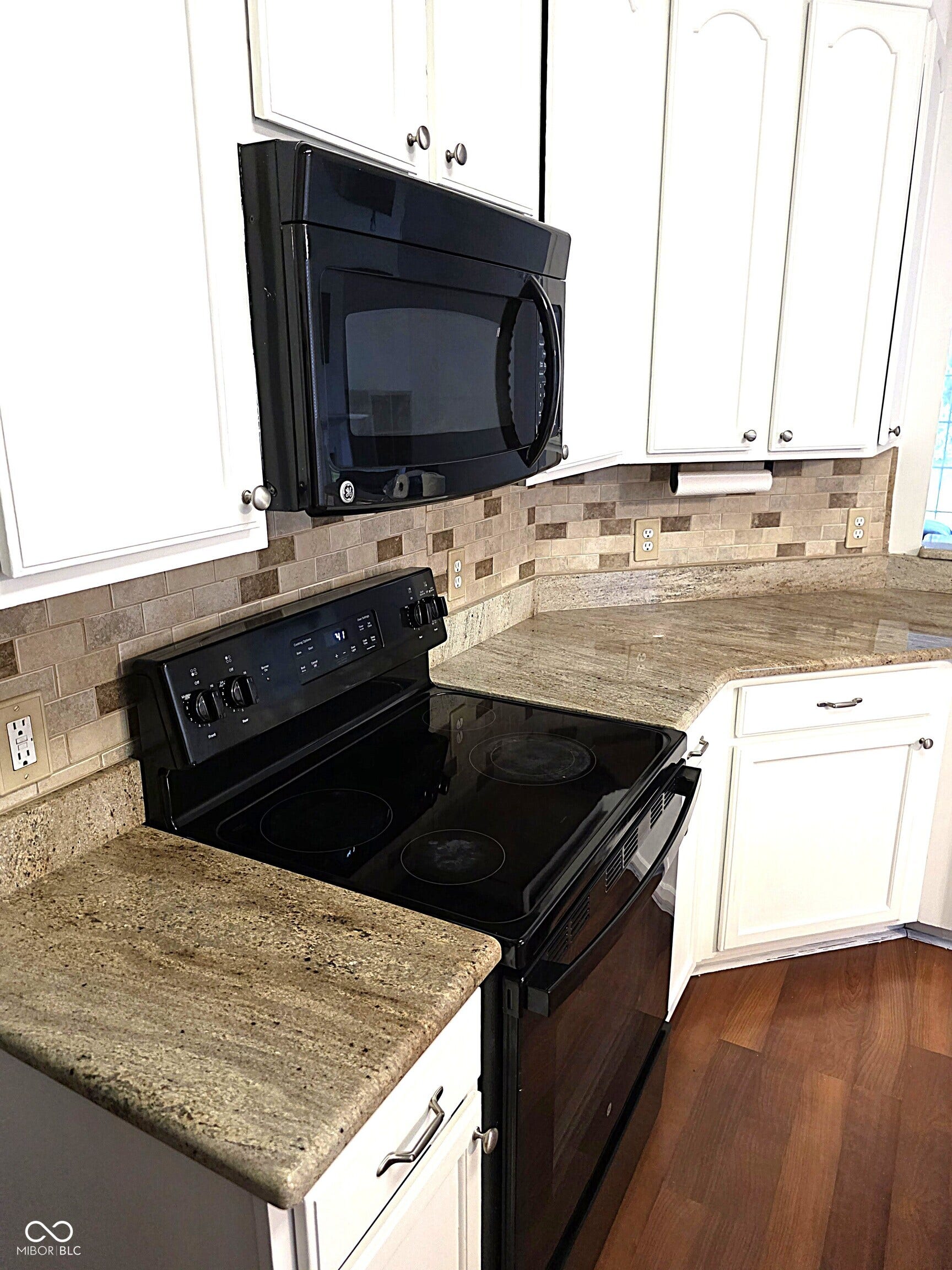 Kitchen featuring white cabinetry, stone countertops, a tile backsplash, and wood-finish flooring