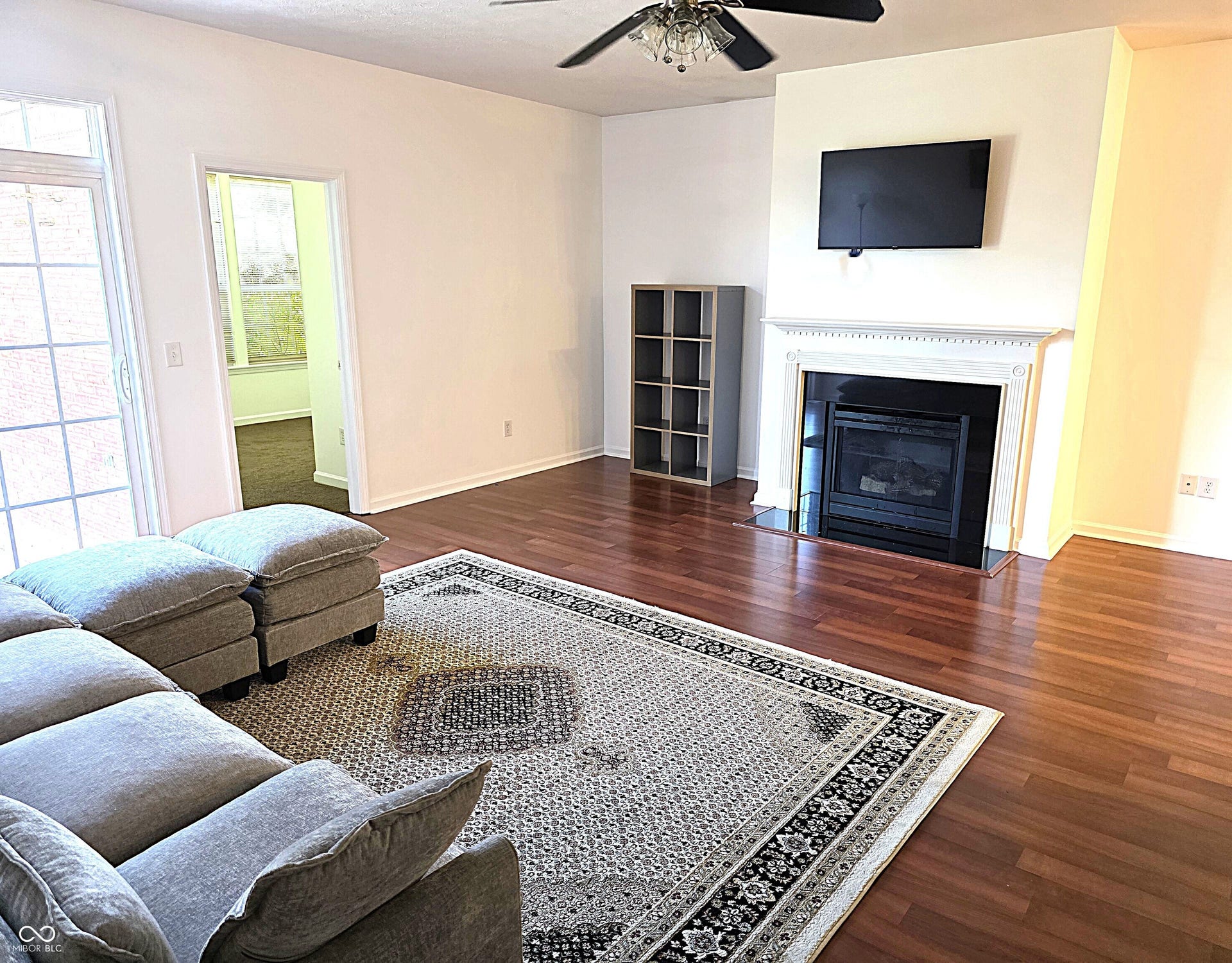 Spacious living area featuring wood-finish flooring, a decorative ceiling fan, and a fireplace with a traditional mantel
