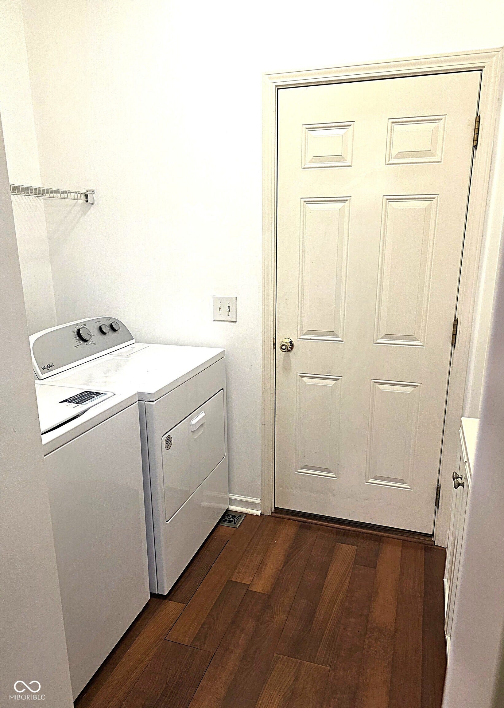 Wood-finish flooring with baseboard trim, white paneled door, and a wall-mounted wire shelf and vanity sink
