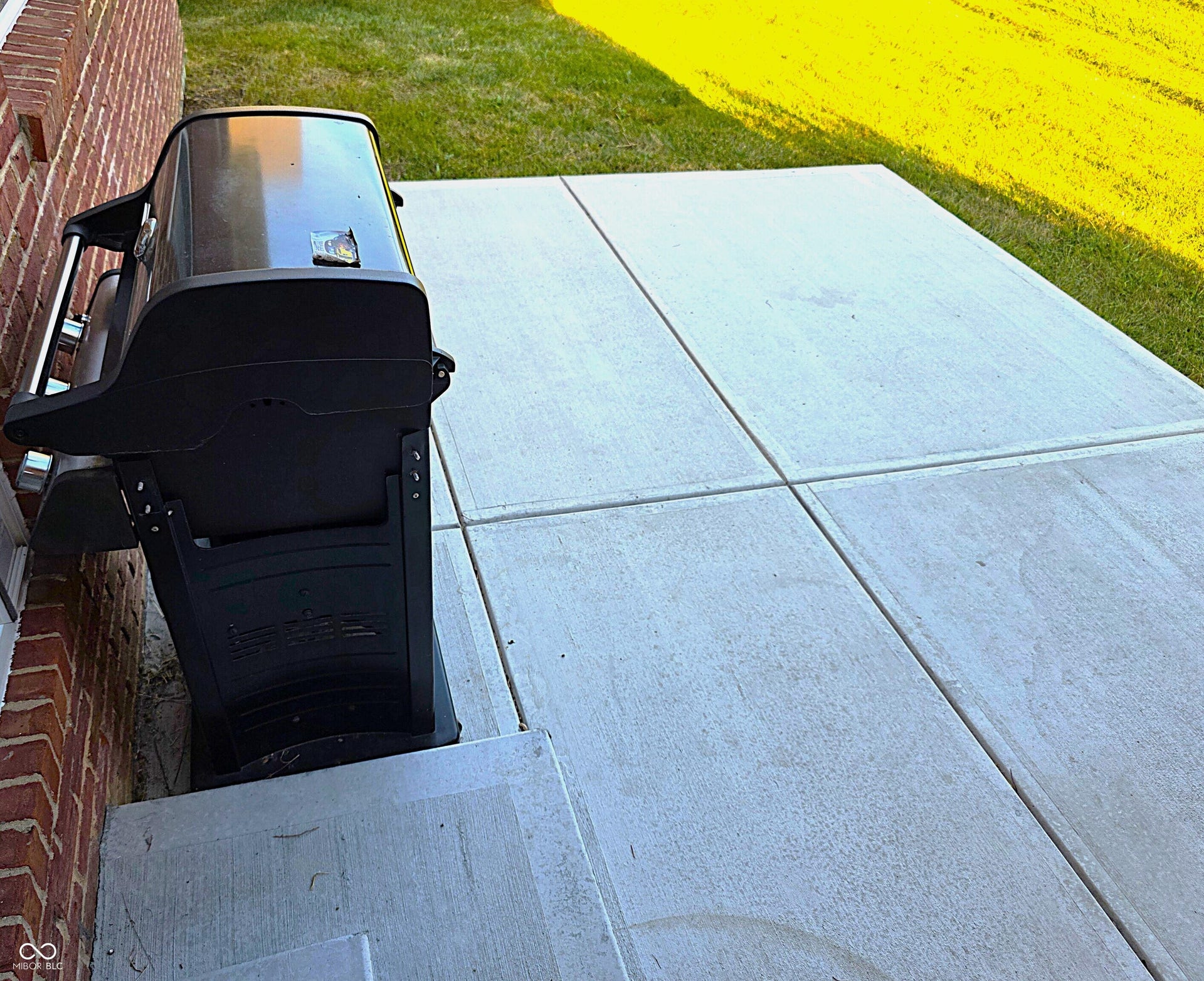 Concrete patio featuring a brick exterior wall and a grass lawn includes grill