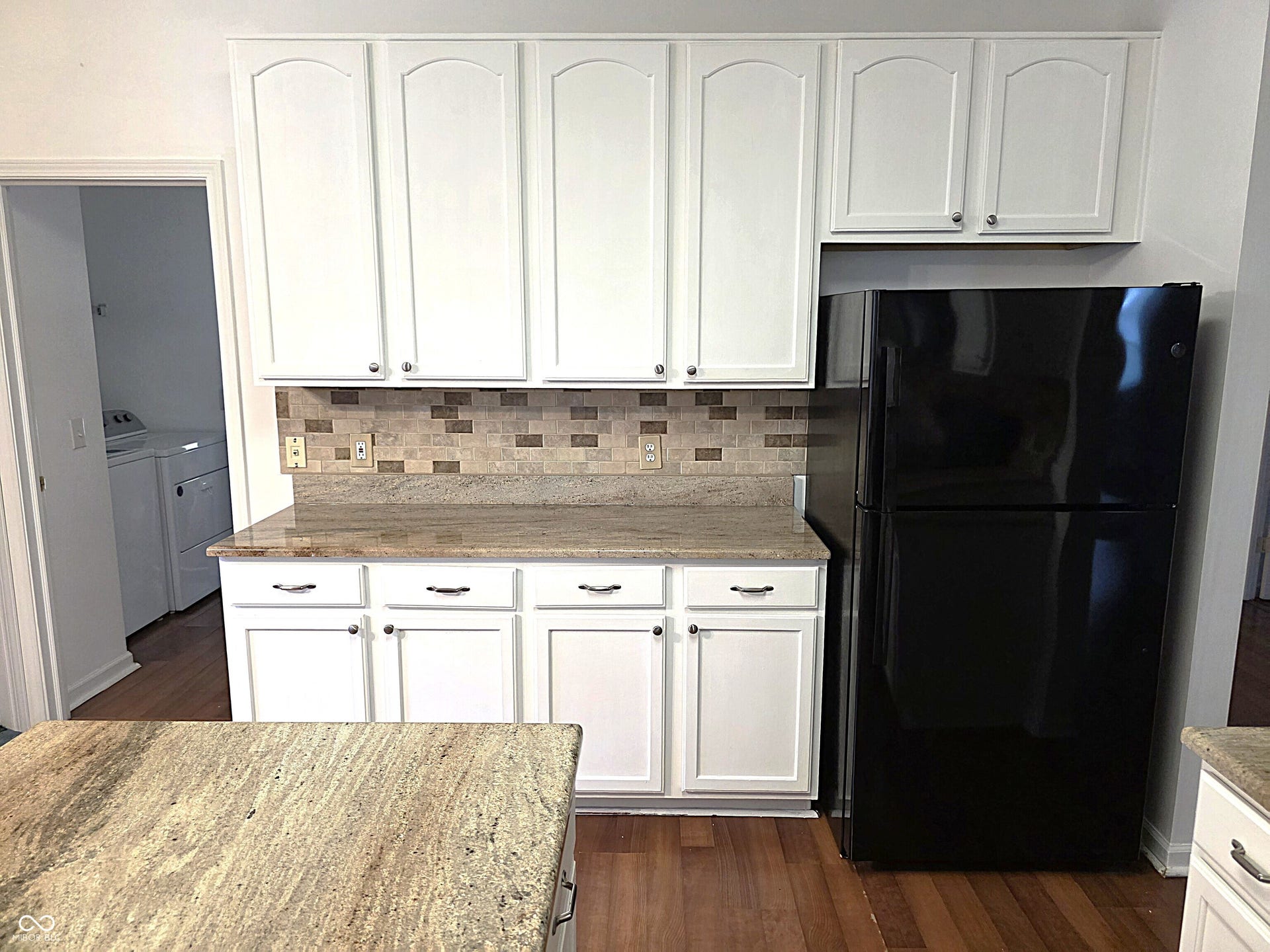 White upper and lower cabinetry, granite countertops, decorative tile backsplash, and wood-finish flooring