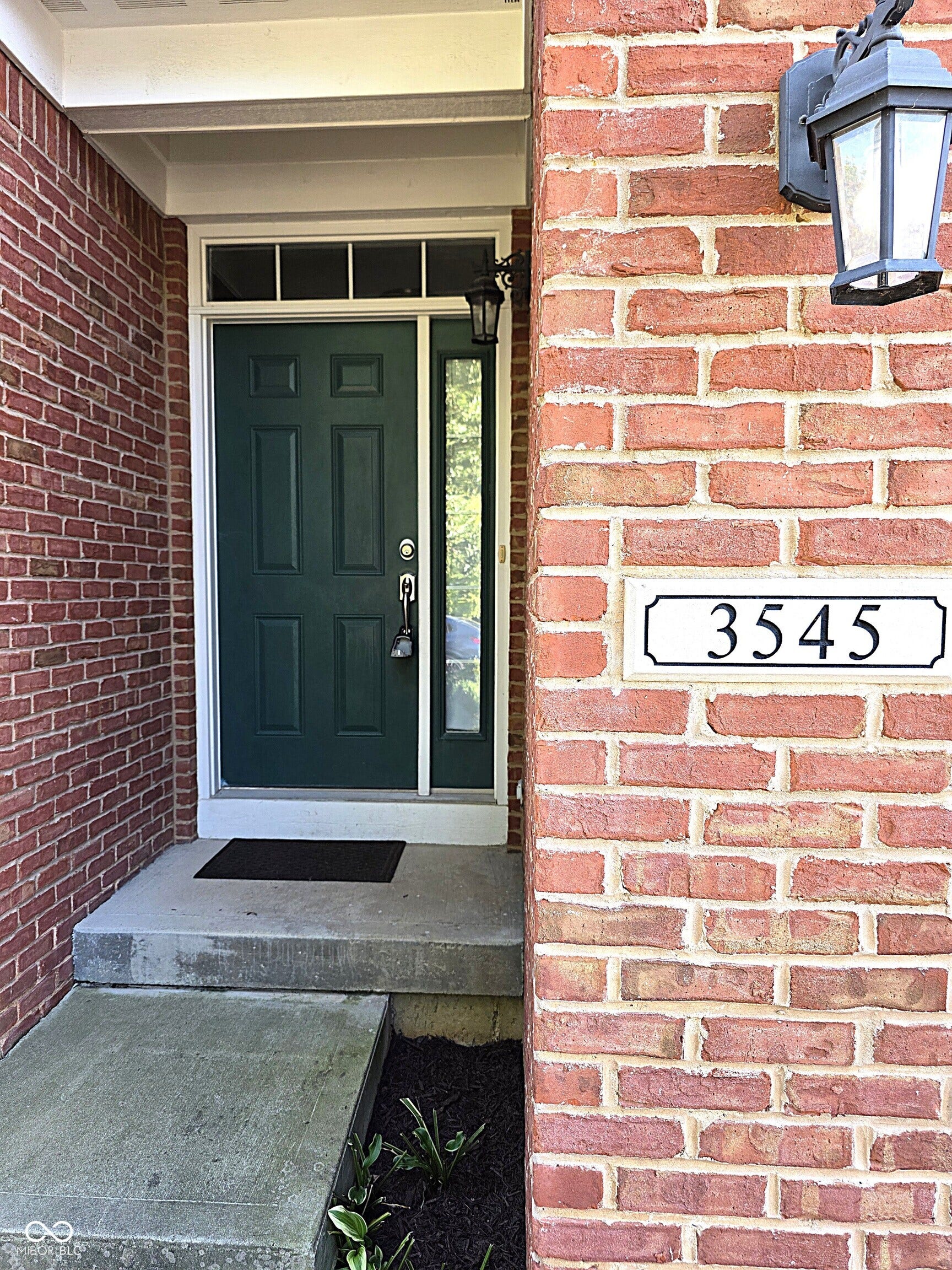 Brick exterior facade featuring a dark green entry door, transom window, and a side light panel