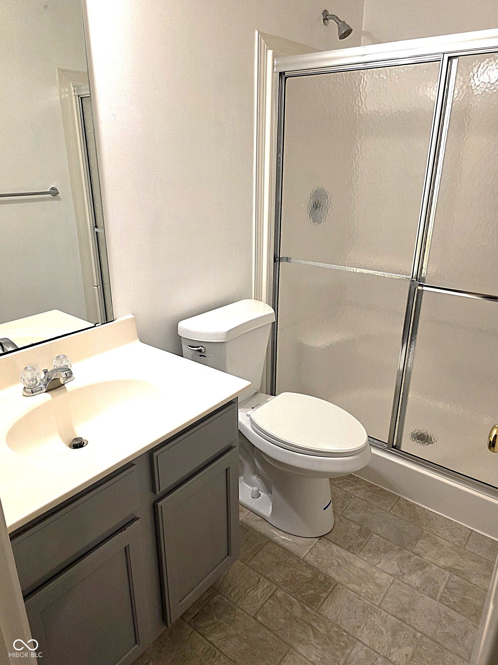 Tiled flooring, vanity with integrated sink, shower with sliding glass enclosure, and toilet