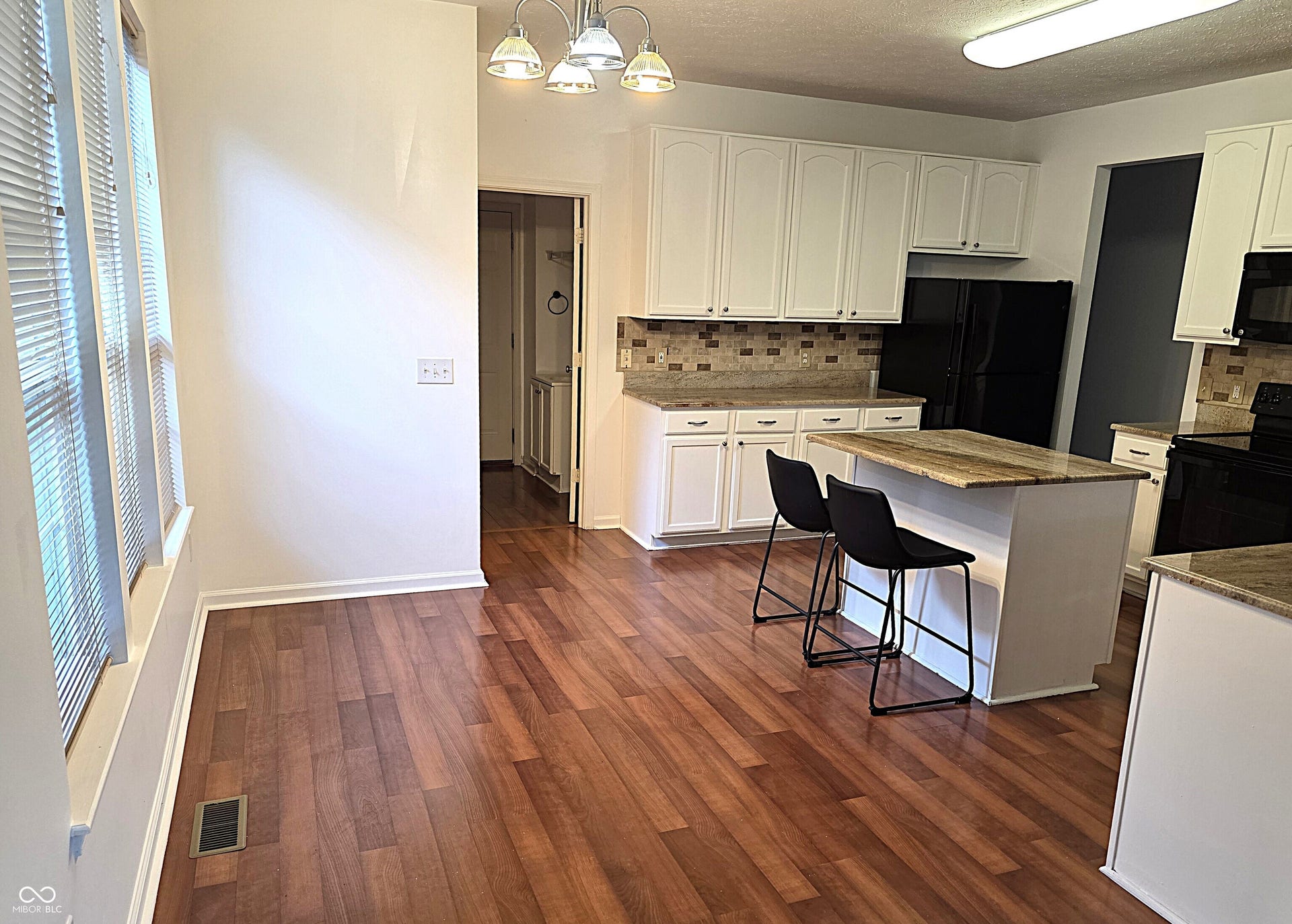 Kitchen featuring wood-finish flooring, white cabinetry, granite countertops, tile backsplash, and a central island with a breakfast bar