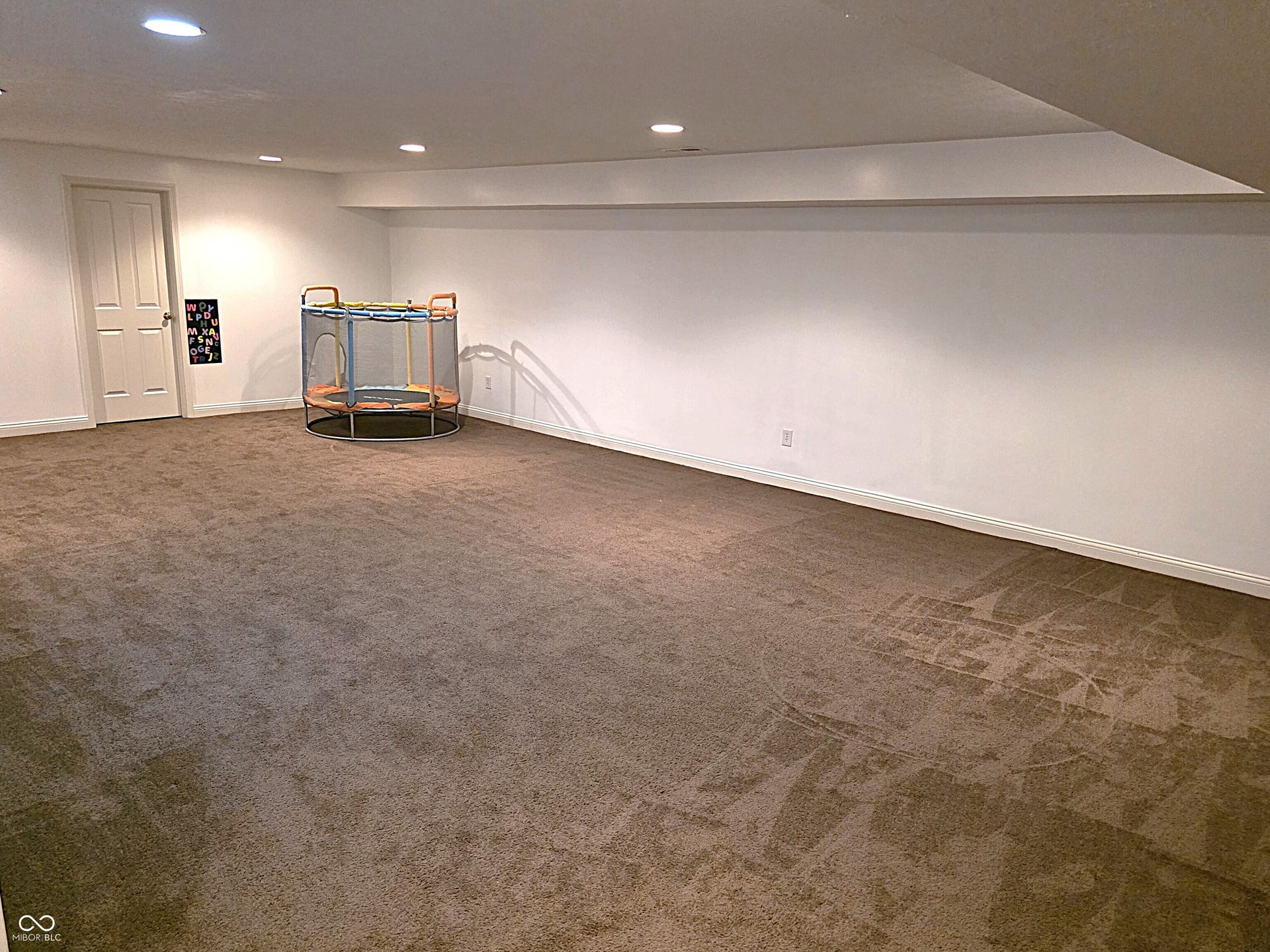 Expansive carpeted room with recessed lighting and a paneled interior door