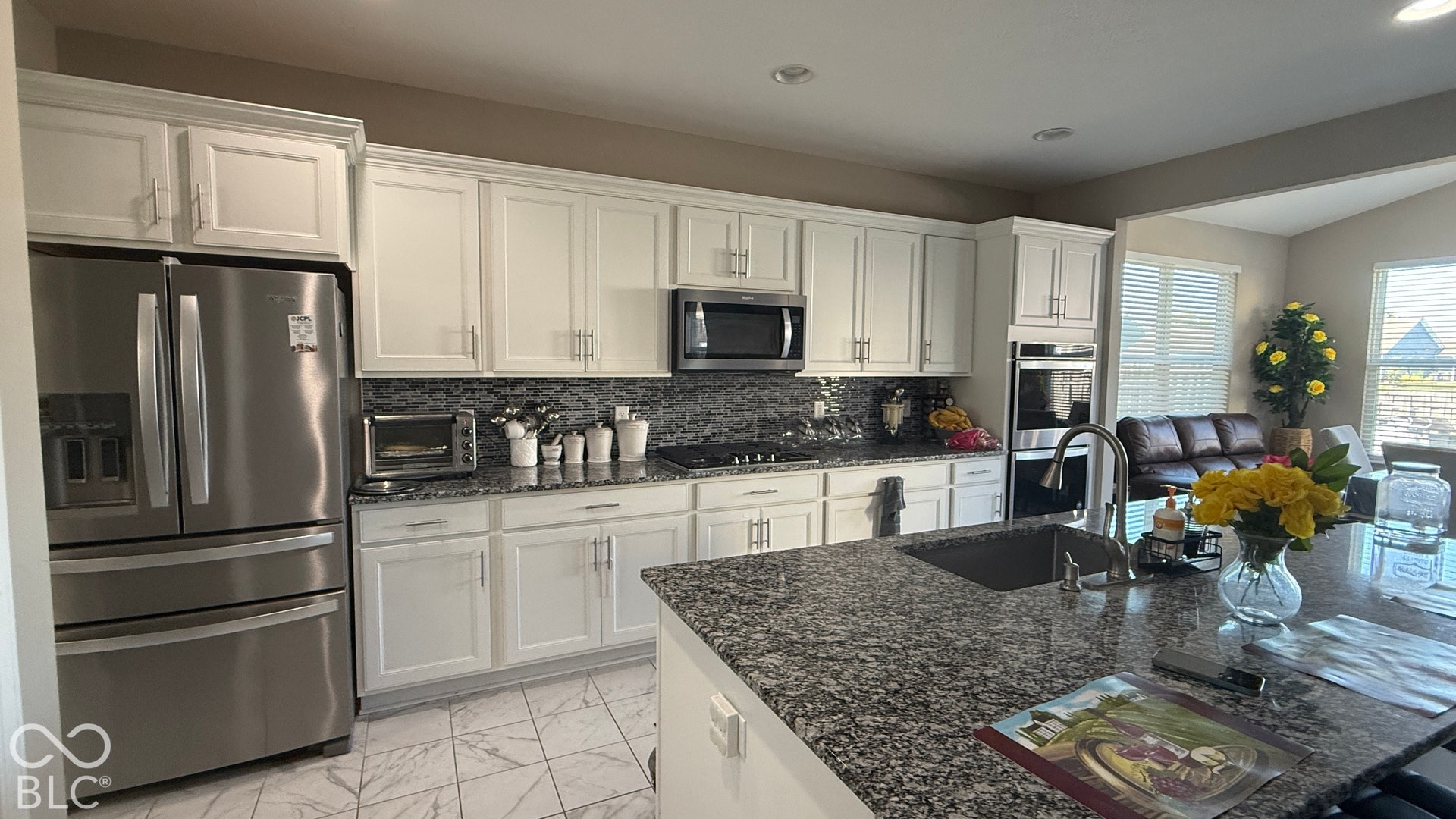 White cabinetry with brushed nickel hardware, stainless steel appliances, speckled stone countertops, tiled backsplash, and recessed lighting