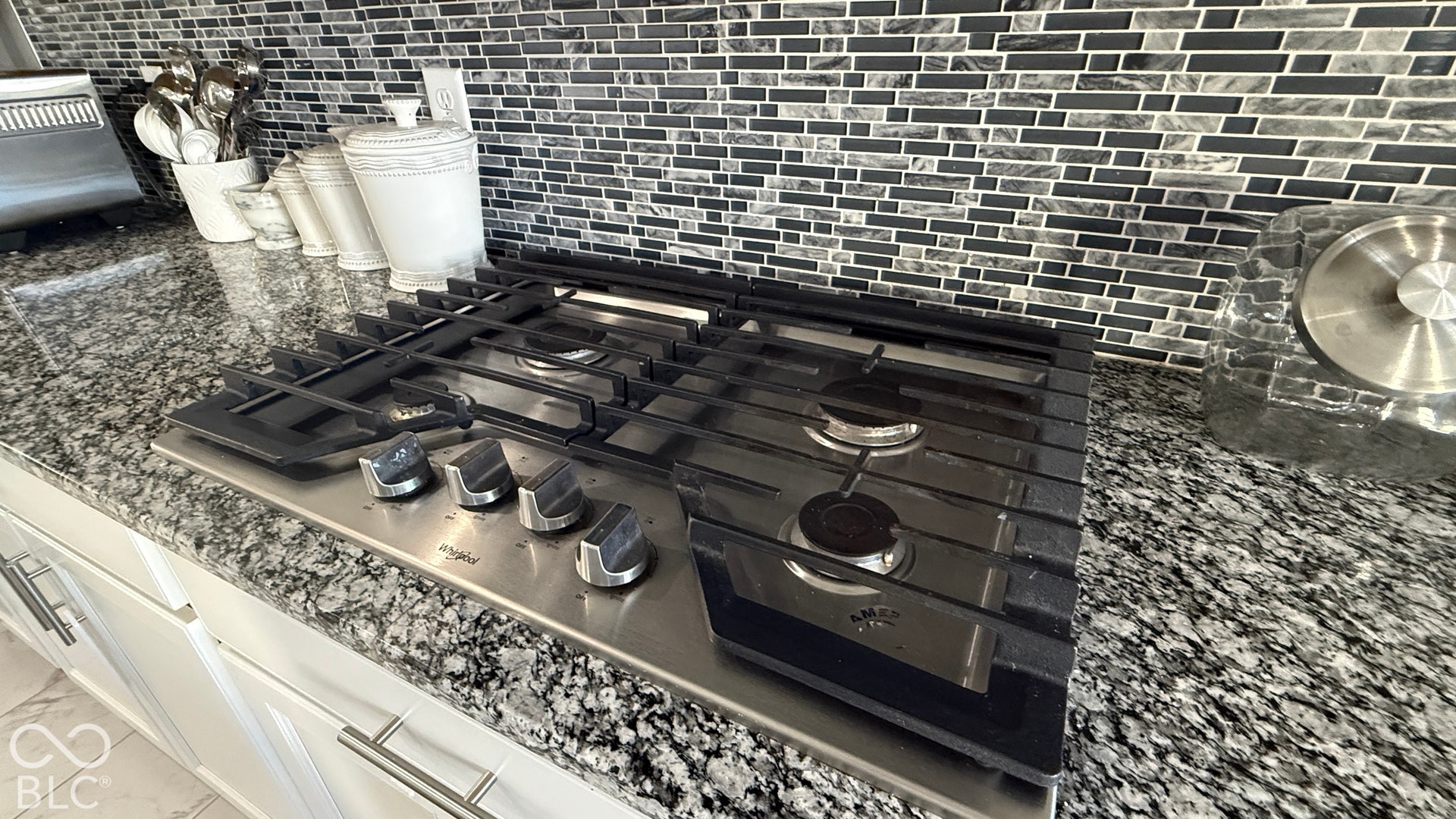 Built-in gas cooktop with stainless steel finish, set into a granite-look countertop, complemented by a mosaic tile backsplash