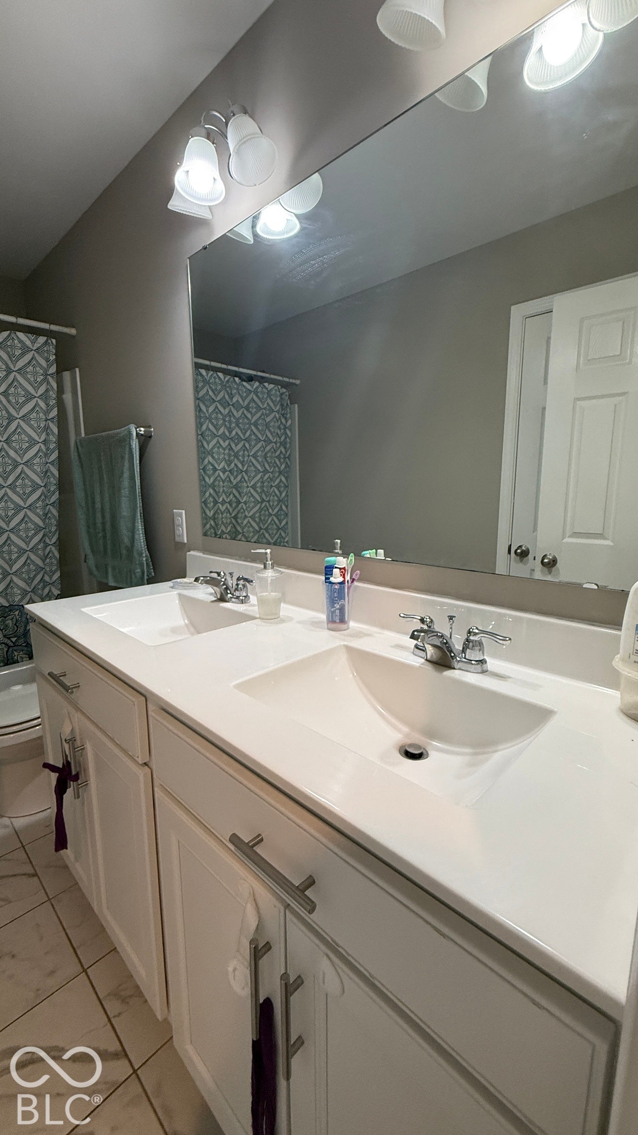Double vanity with integrated sinks and white cabinetry, featuring brushed nickel hardware, a large wall-mounted mirror, and tile flooring