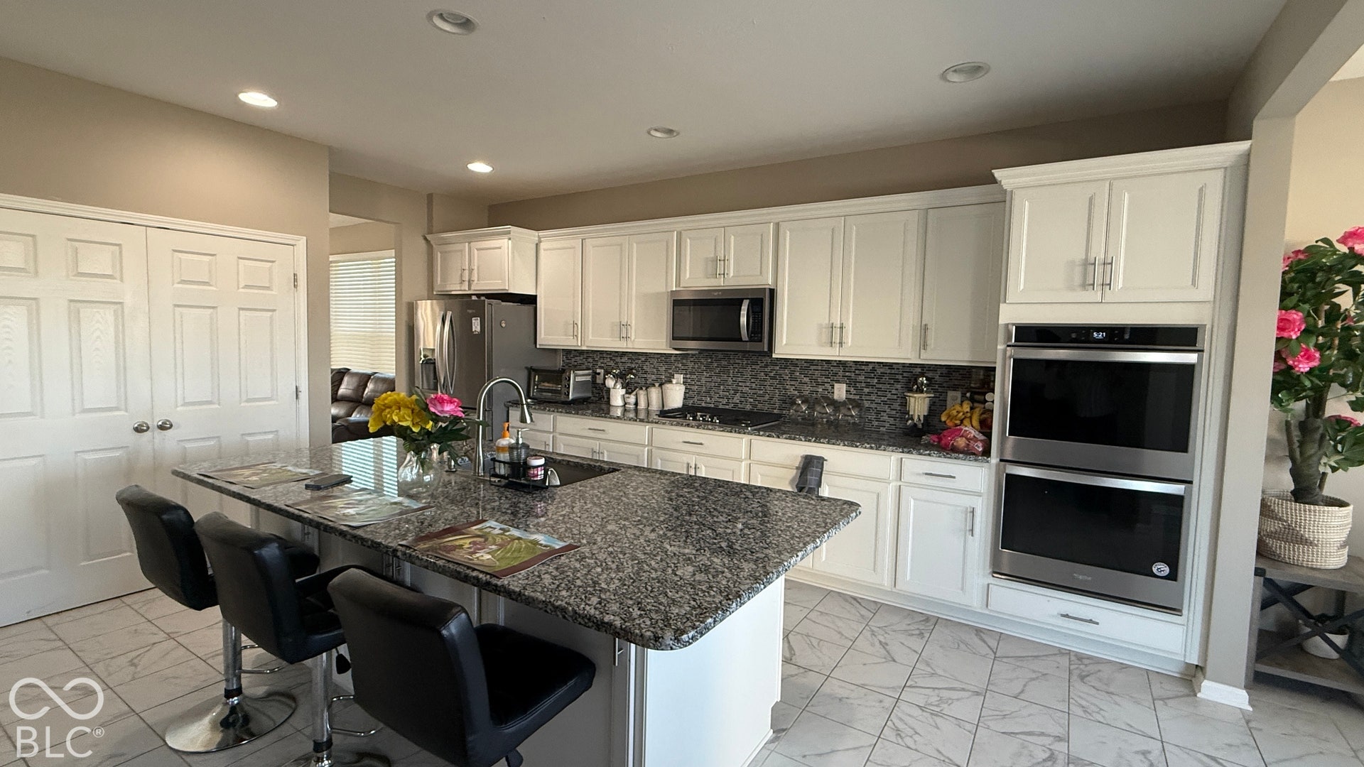Spacious kitchen featuring an expansive granite-top island, white cabinetry, stainless steel appliances, and tile flooring