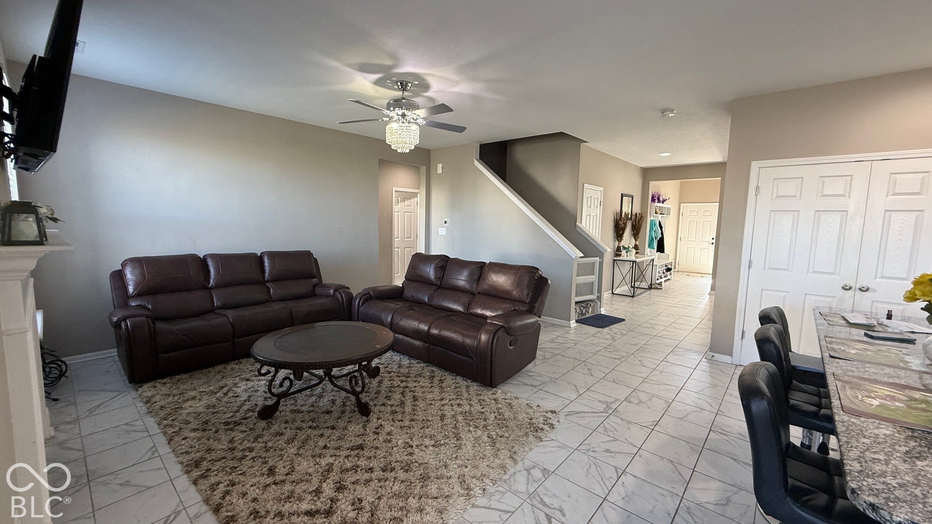 Living area featuring light gray walls, white tile flooring, a white mantel, and a decorative ceiling fan with lighting