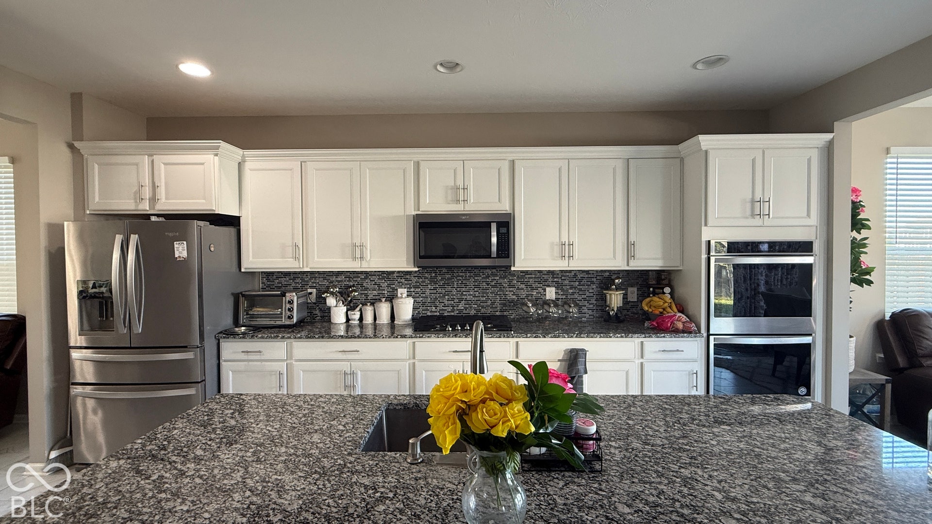 Kitchen featuring a large island with an undermount sink, granite countertops, white cabinetry, and stainless steel appliances including a built-in double oven