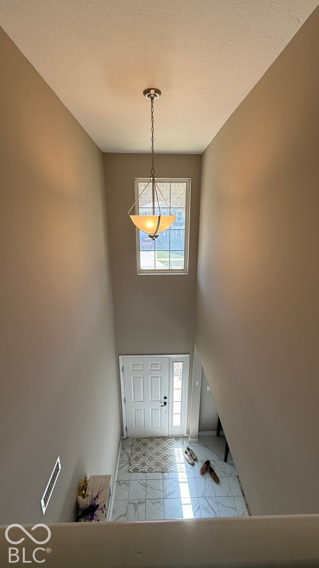 Two-story foyer with high ceilings, featuring a transom window, a white paneled entry door, and large format tile flooring