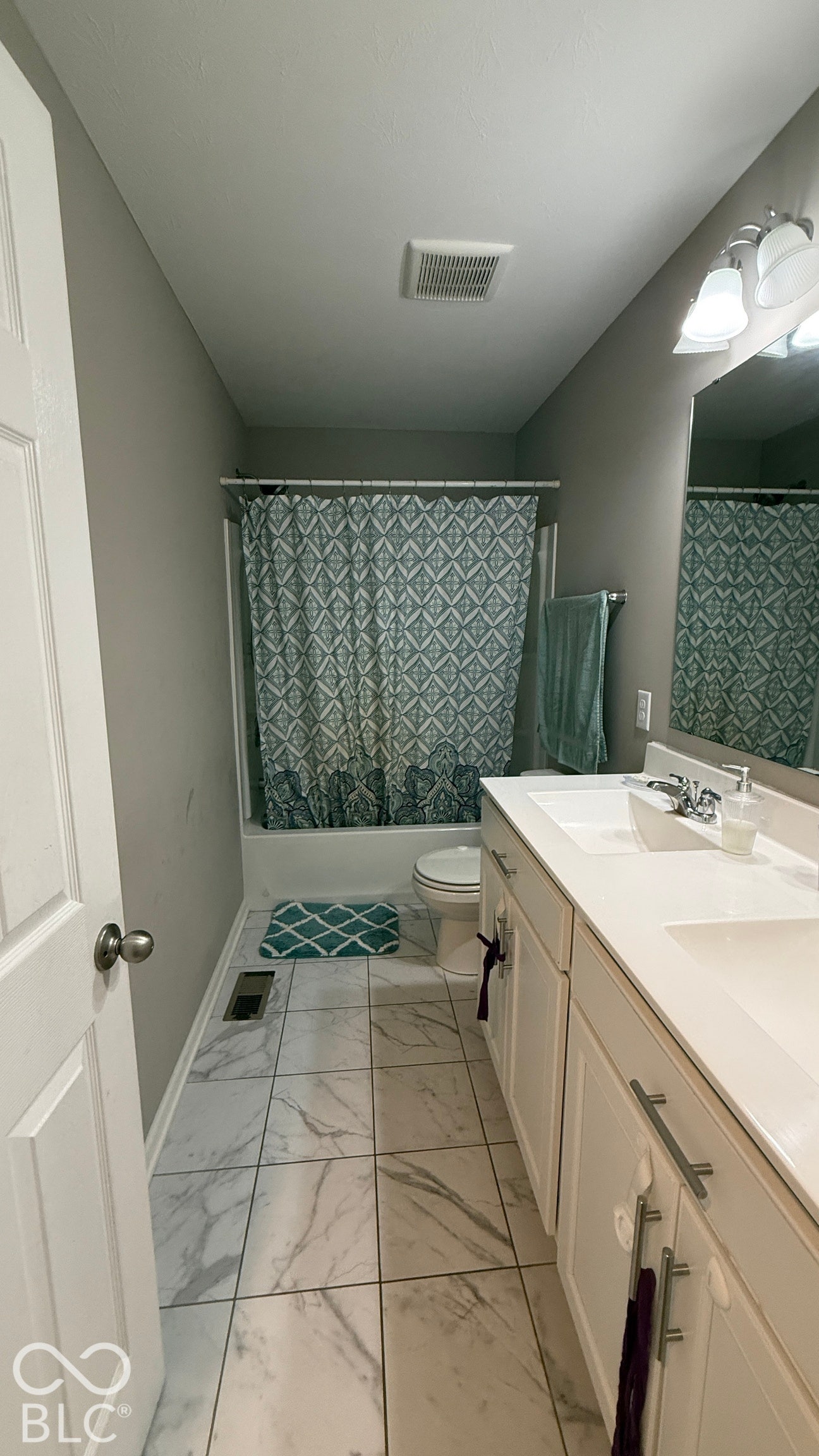 Dual vanity with white cabinetry and chrome hardware, a built-in tub with shower, and tiled flooring