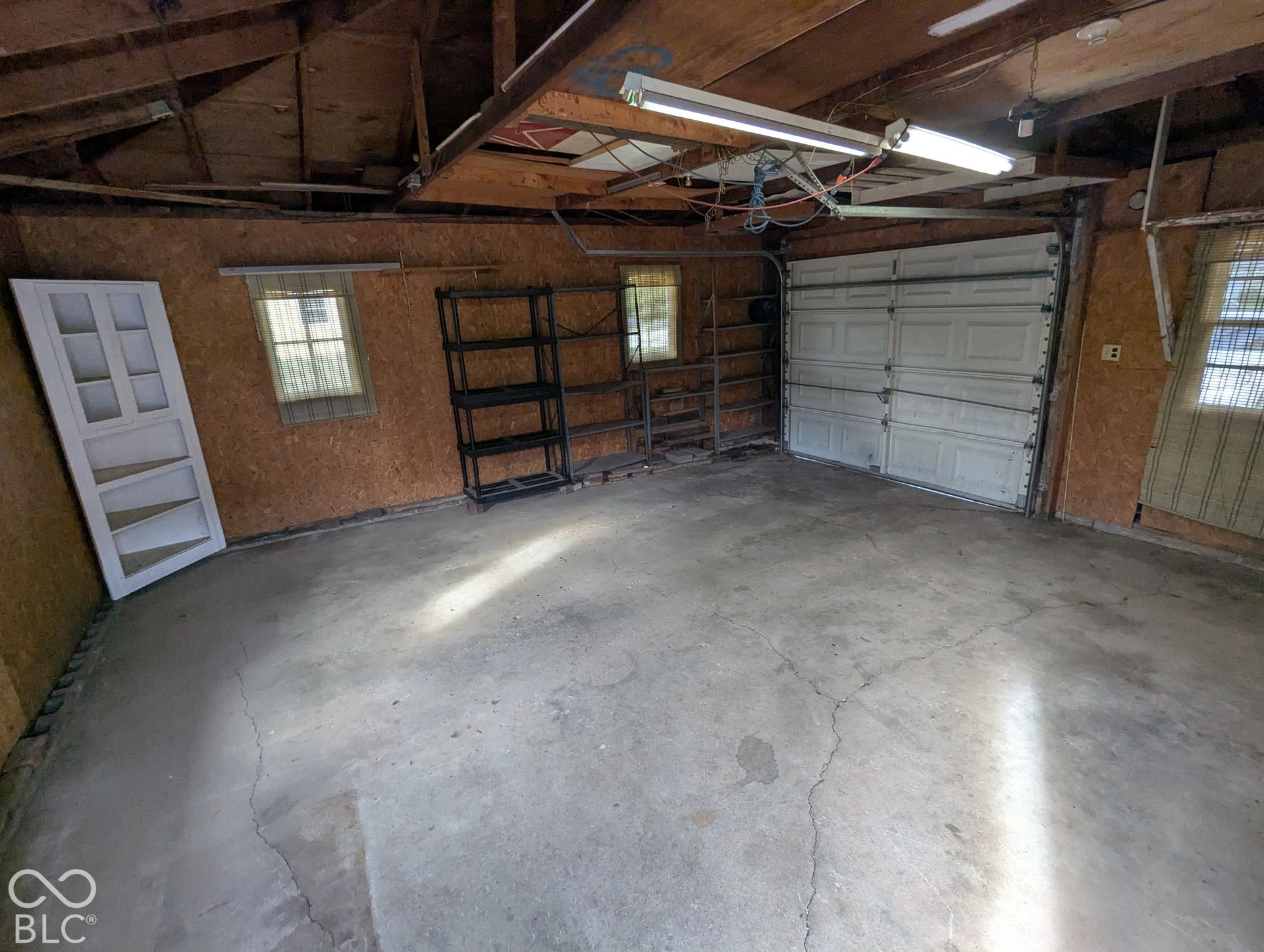 364 Robbins Drive, Greenwood, IN 46142 Oversized 1 car Garage interior featuring exposed wooden ceiling joists, oriented strand board wall paneling, dual-pane windows, and linear fluorescent overhead lighting