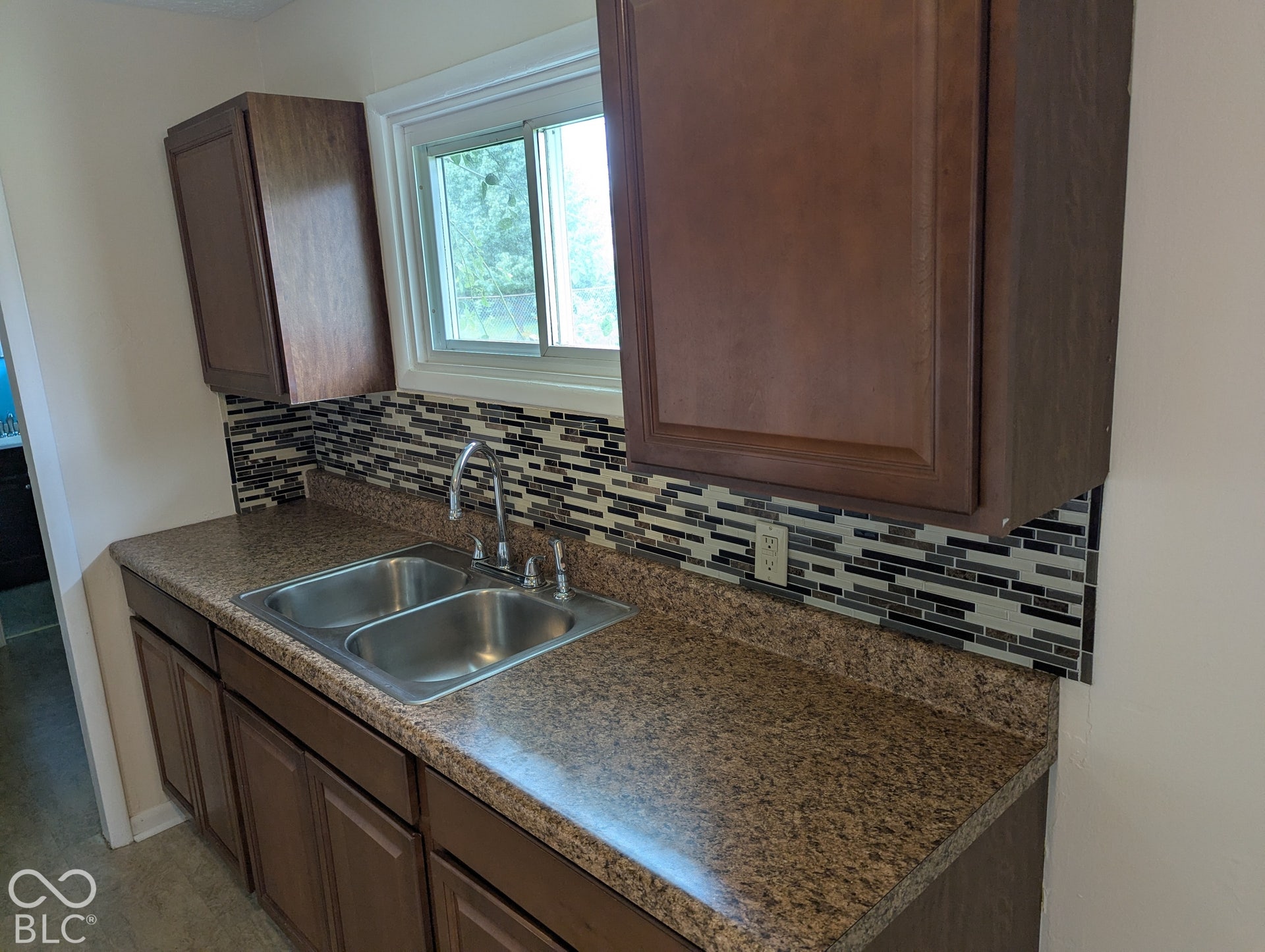 364 Robbins Drive, Greenwood, IN 46142 Kitchen featuring dark wood-finish cabinetry, solid-surface countertops, dual-basin stainless steel sink with high-arc faucet, and multi-tone glass tile backsplash