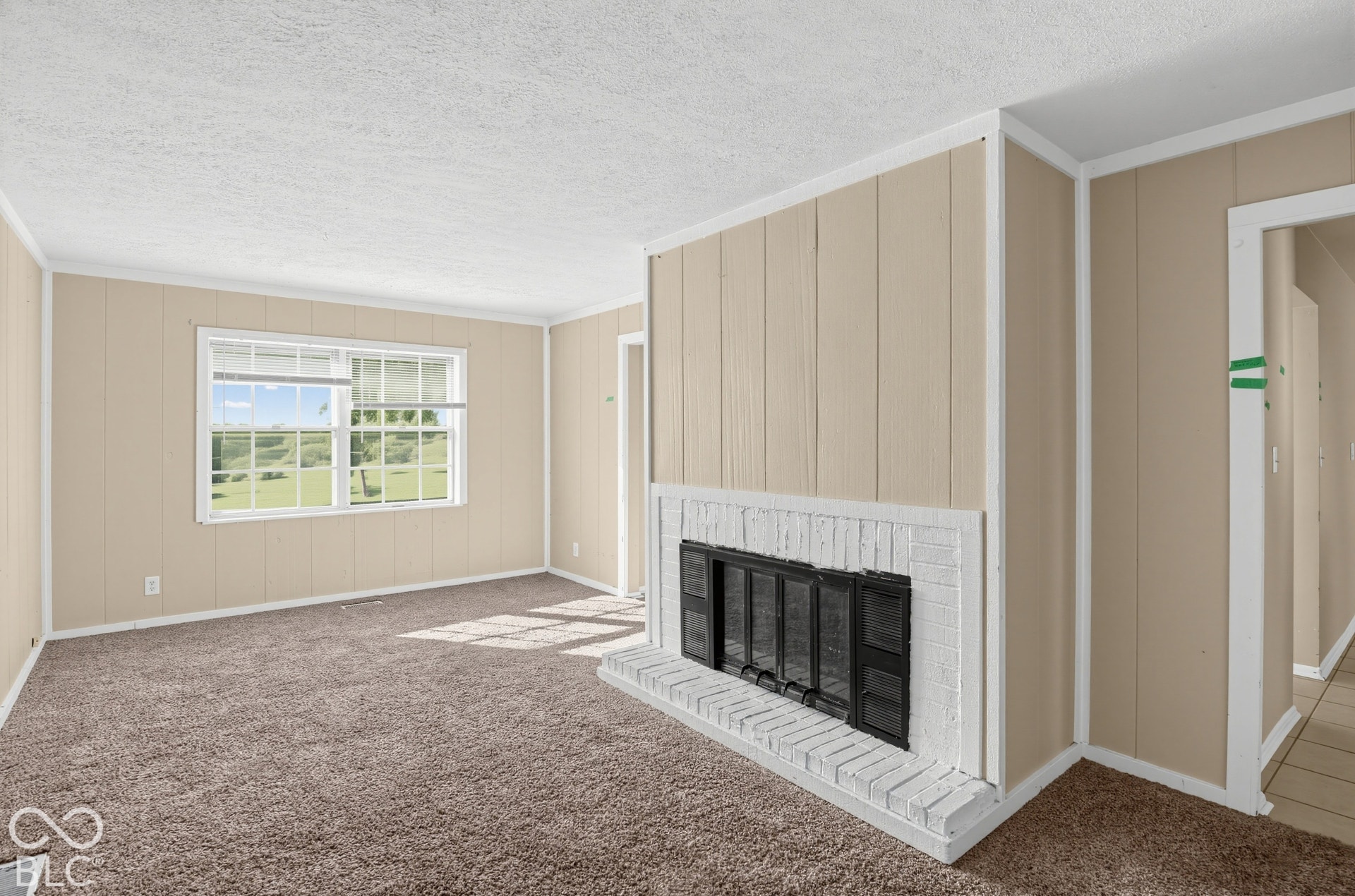3733 Ireland Drive, Indianapolis, IN 46235 Wall-to-wall carpeting, window with outdoor scenery, painted vertical paneling, white brick fireplace with black metal insert, and textured ceiling