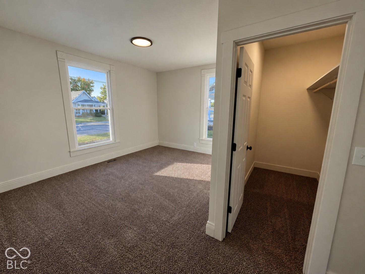 Carpeted flooring, two windows with white trim, built-in closet, flush-mount ceiling light fixture, and neutral wall paint
