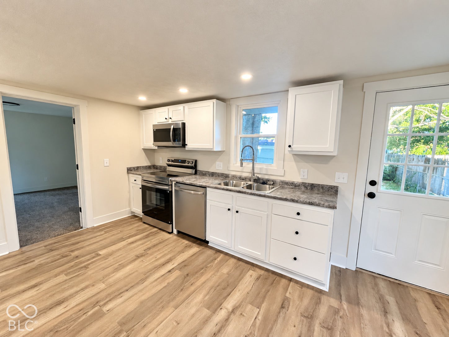 Wood-finish flooring, white cabinetry, stainless steel appliances, recessed lighting, and a kitchen sink with a gooseneck faucet