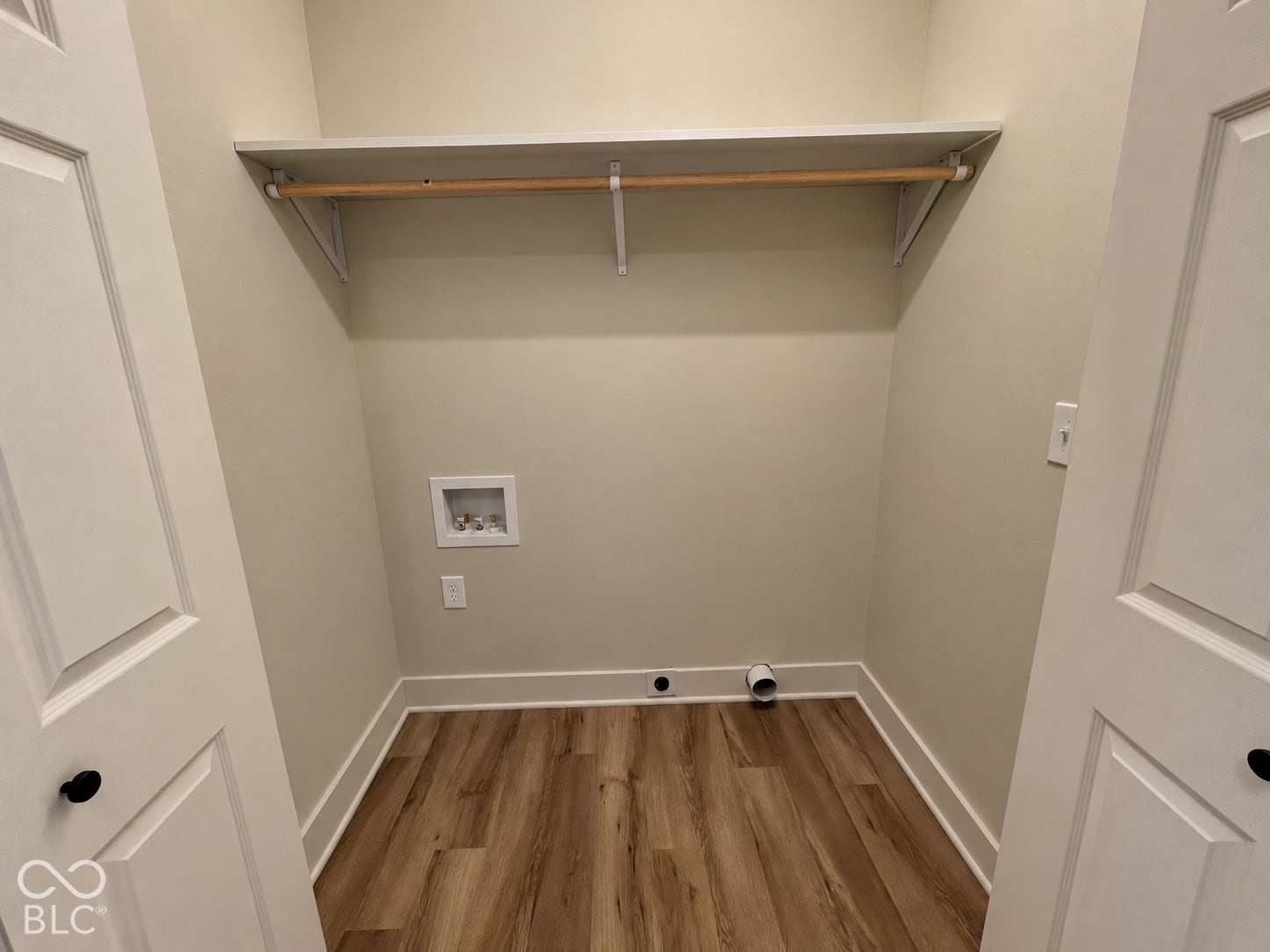 Laundry area featuring wood-finish flooring, a built-in shelf with hanging rod, and wall-mounted utility connections