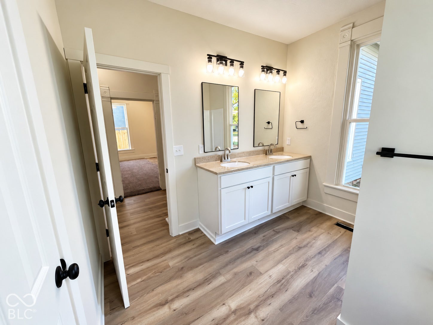 Dual vanity with undermount sinks, wood-finish flooring, and a window with decorative trim