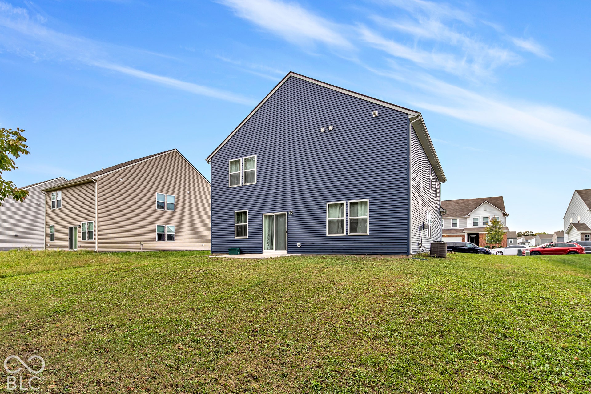 Rear exterior featuring blue horizontal siding, multiple windows, and a sliding glass door opening to a concrete patio