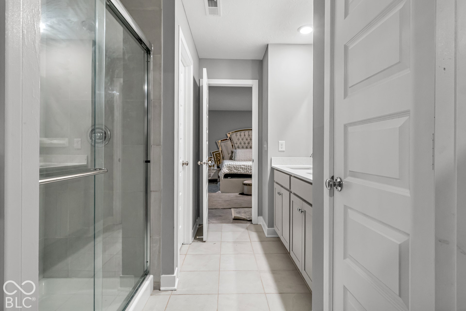 Glass-enclosed shower with chrome fixtures, dual-sink vanity with white countertop, and tiled flooring