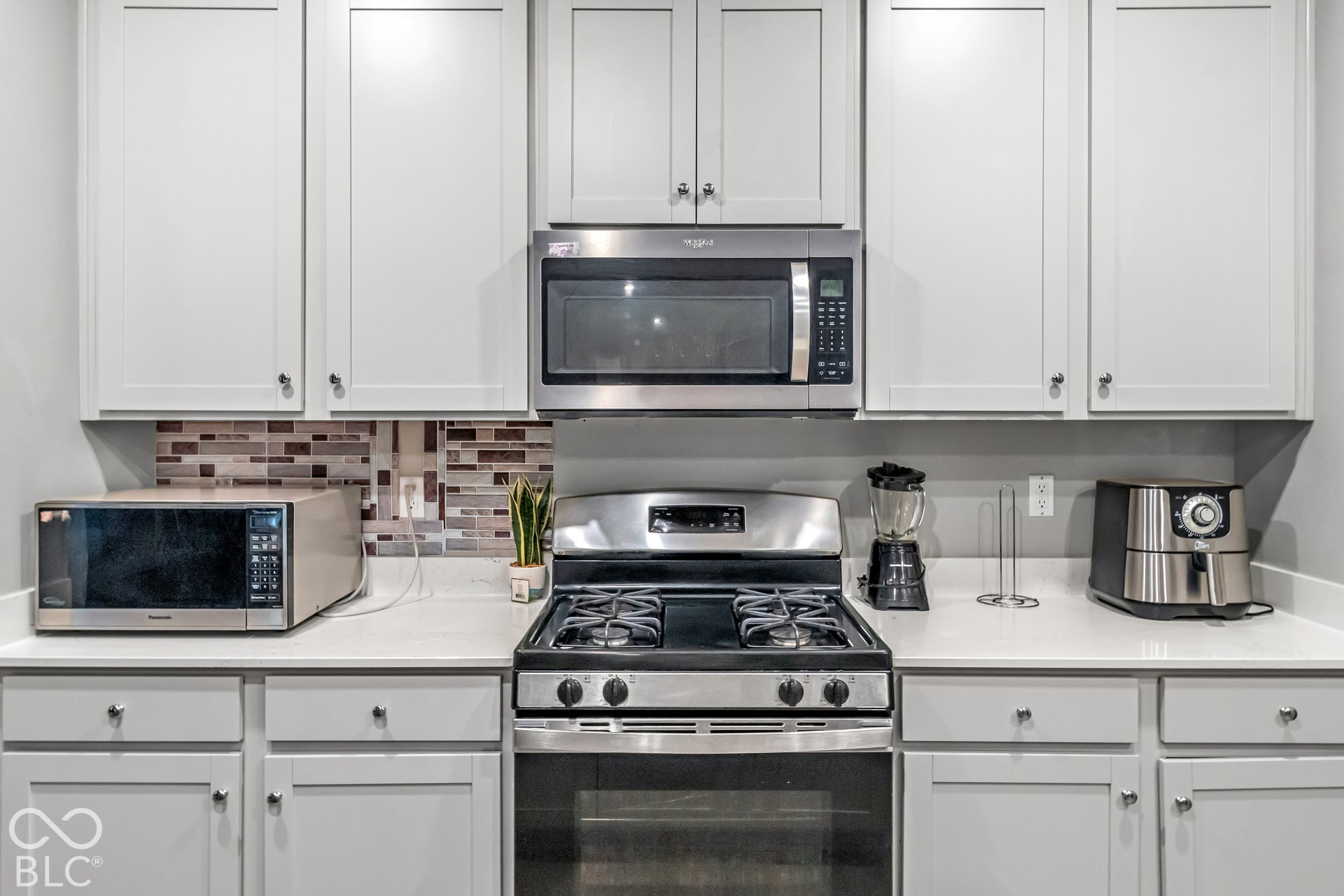 White shaker-style cabinetry with dark hardware, stainless steel gas range, quartz countertops, and a mosaic tile backsplash