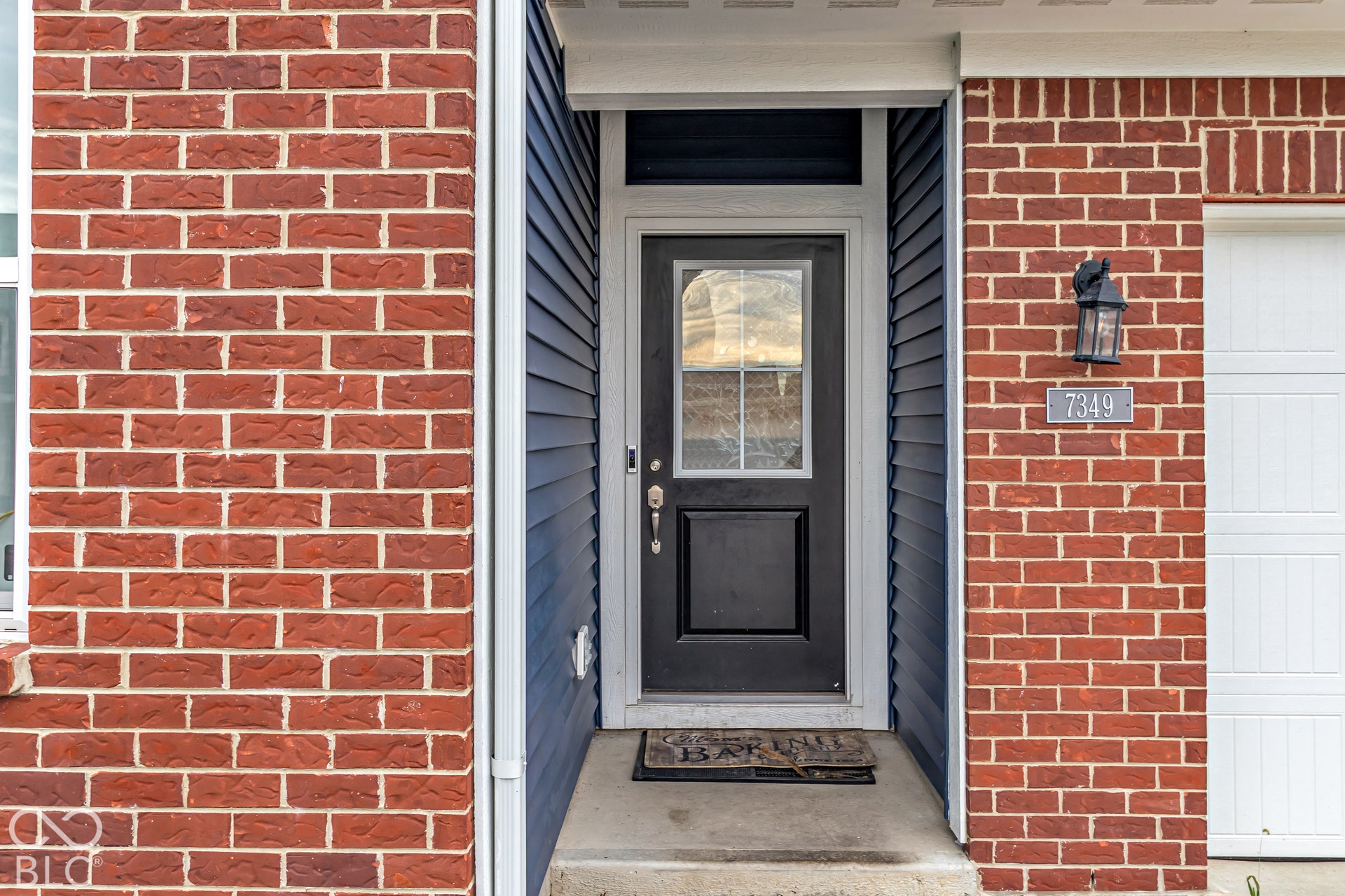 Brick and siding exterior featuring a black front door with an upper window pane, exterior wall lantern, and a white garage door
