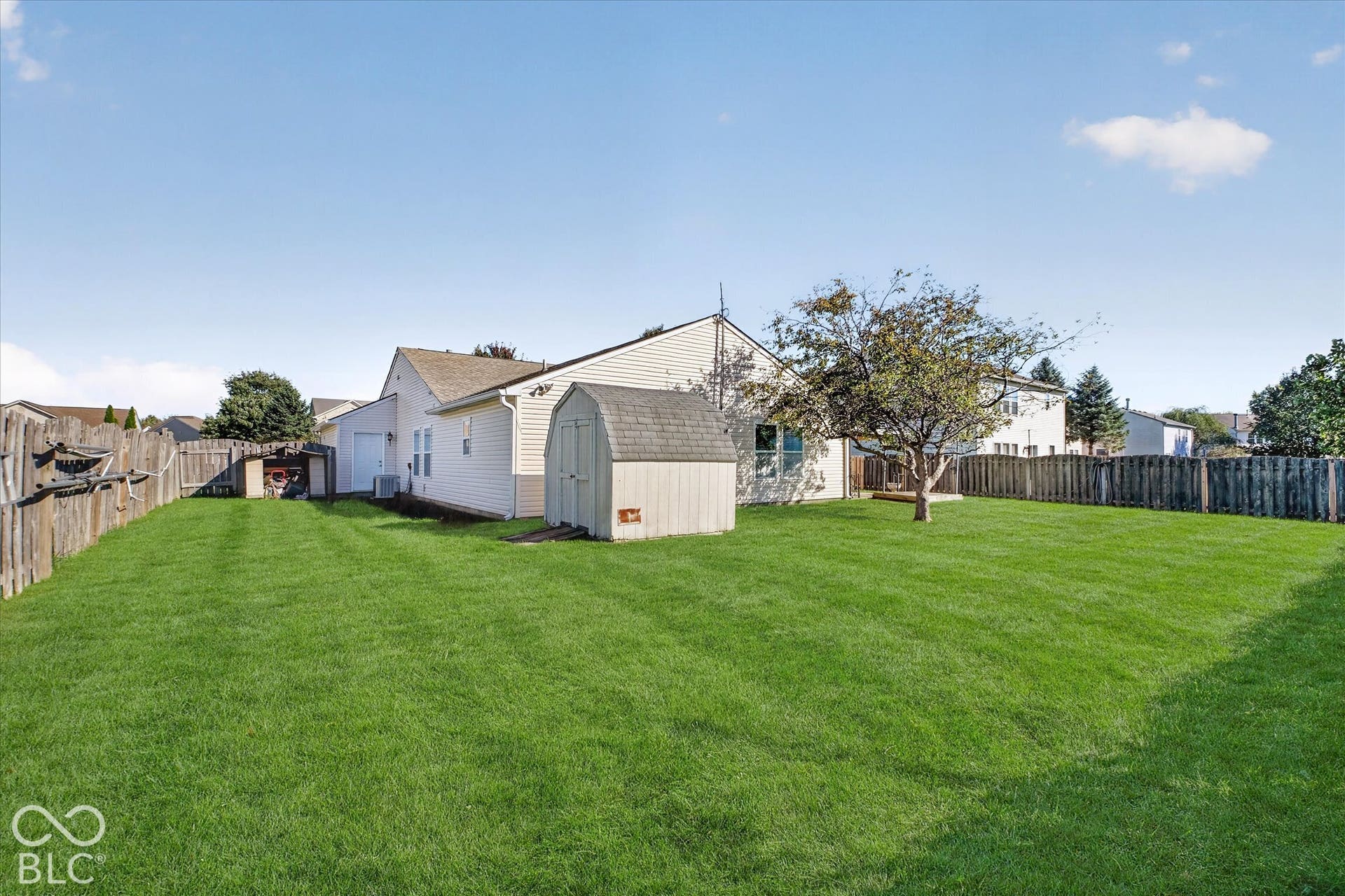 12980 Coyote Run, Fishers, IN 46038 Expansive green lawn with a wood privacy fence, featuring a storage shed and mature trees