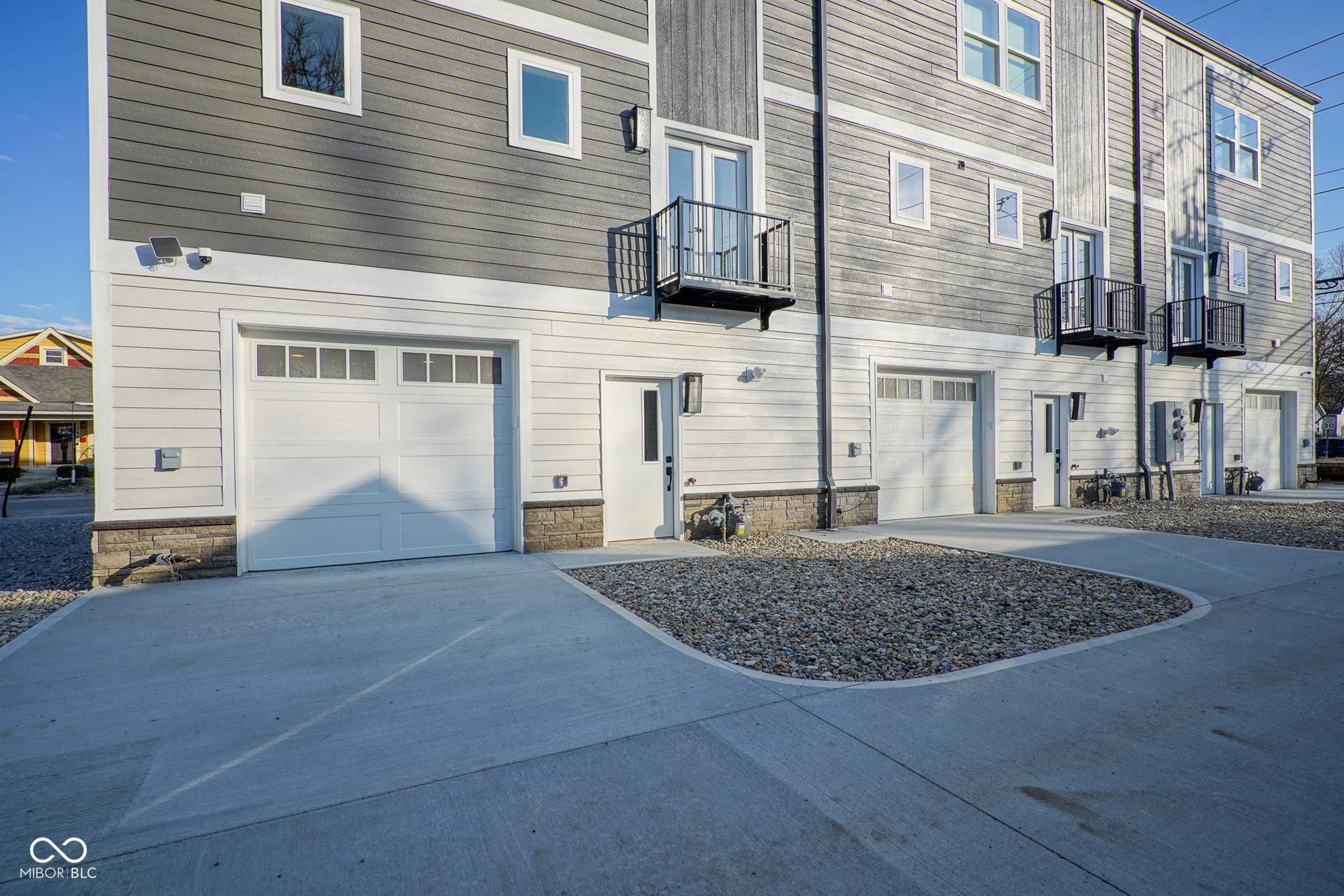 back of property featuring stone siding, driveway, a garage, and a balcony