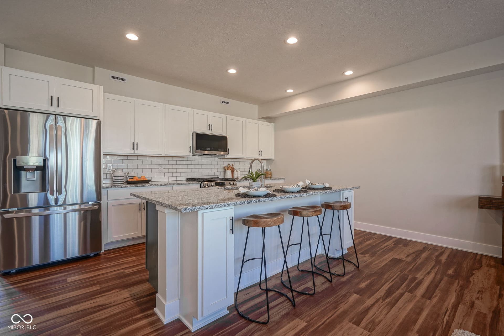 kitchen with appliances with stainless steel finishes, white cabinetry, light stone countertops, a kitchen bar, and recessed lighting