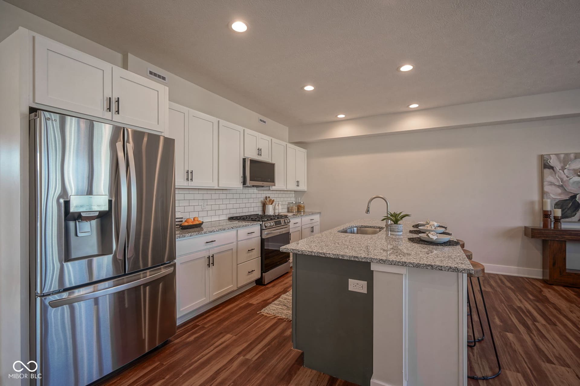 kitchen with stainless steel appliances, white cabinetry, light stone counters, a breakfast bar, and an island with sink