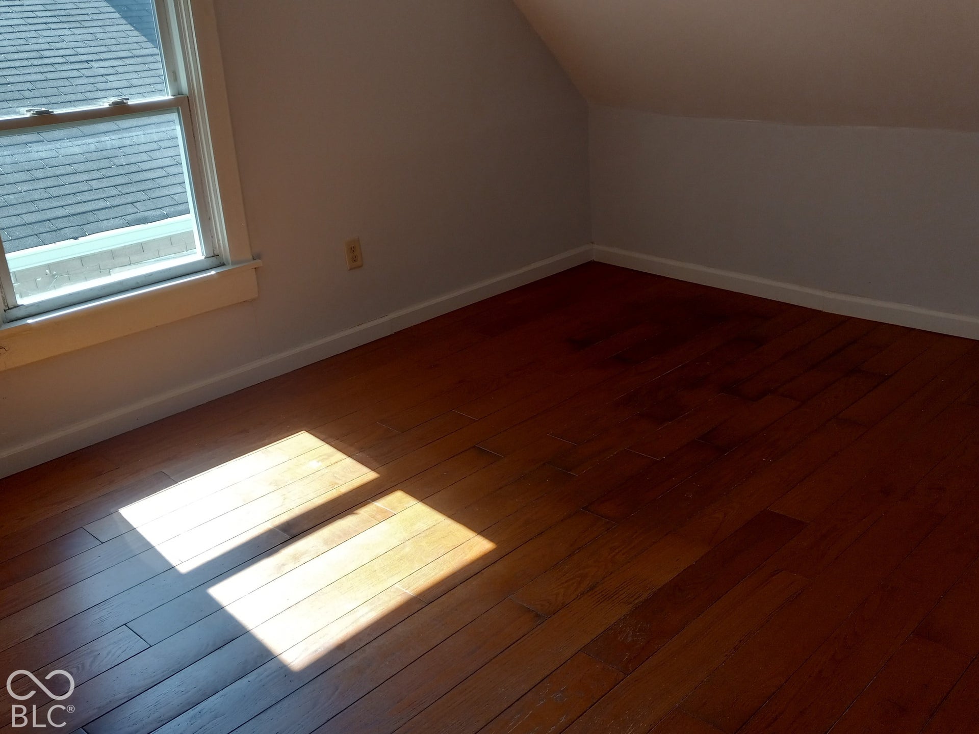 Wood-finish flooring with white trim, angled ceilings, and a double-hung window