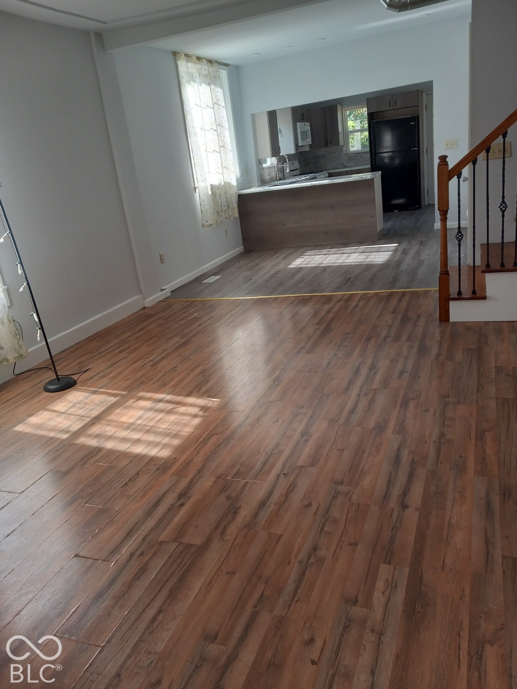 Wood-finish flooring, staircase with dark wood handrail and wrought iron spindles, kitchen with light wood-finish cabinetry, built-in refrigerator, and stone-look countertops