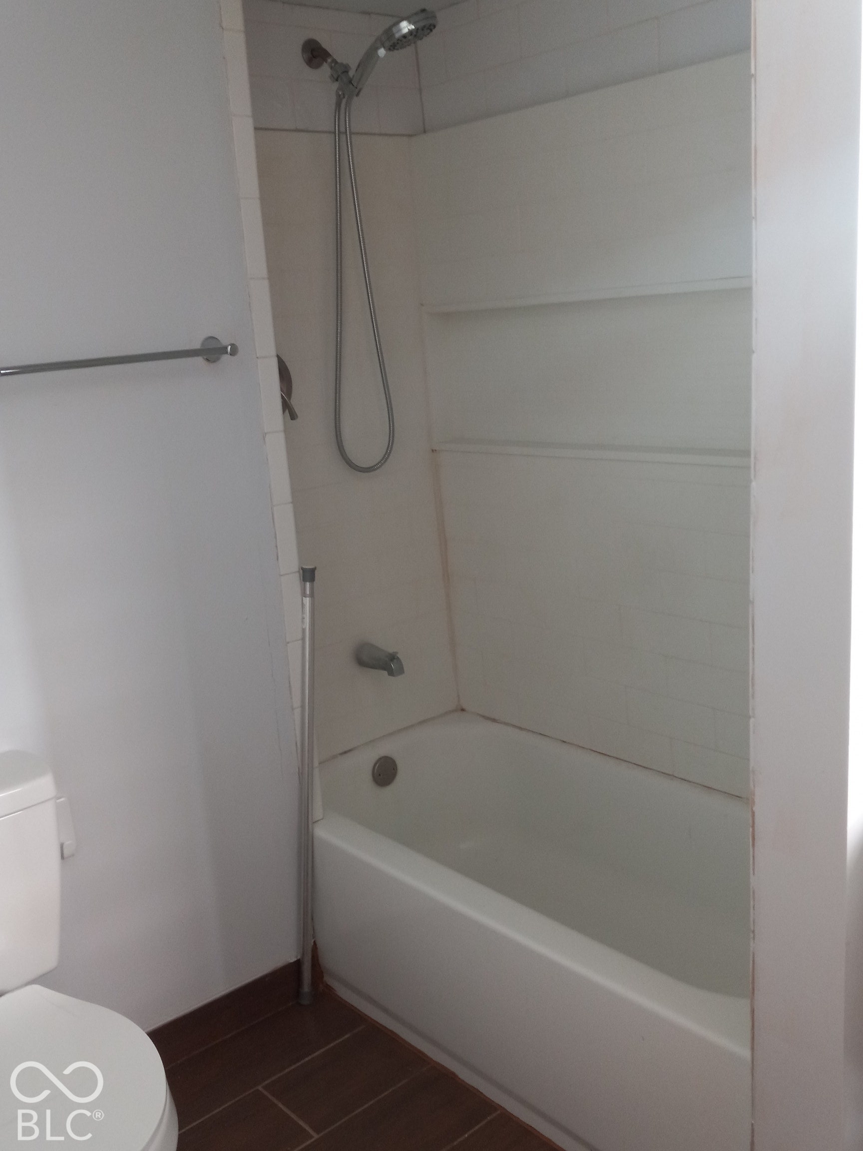 Bathtub with white surround, wall-mounted shower head, and tile-finish flooring