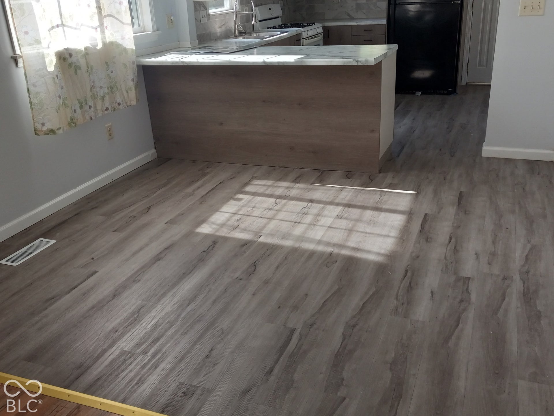 Wood-finish flooring throughout, kitchen island with a light-colored countertop, built-in cabinetry, and a black refrigerator