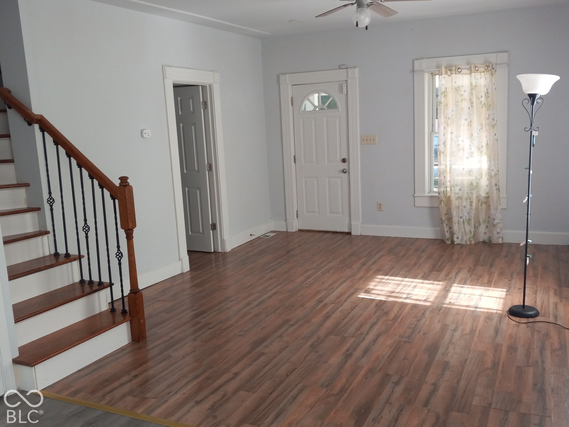 Wood-finish flooring throughout, with a classic white entry door and a staircase featuring wood treads and wrought iron balusters