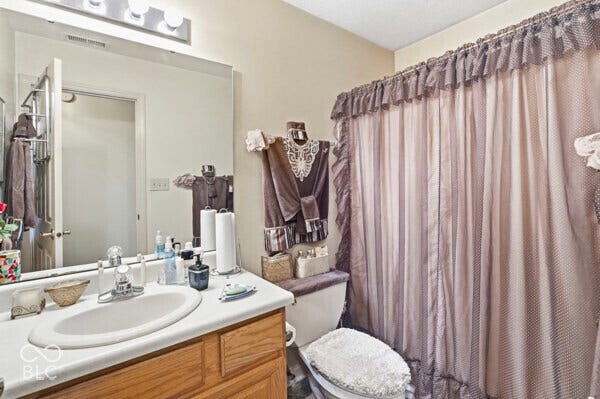 Bathroom featuring a vanity with a white countertop and a drop-in sink, a wall-mounted mirror, and a shower area with a curtain rod