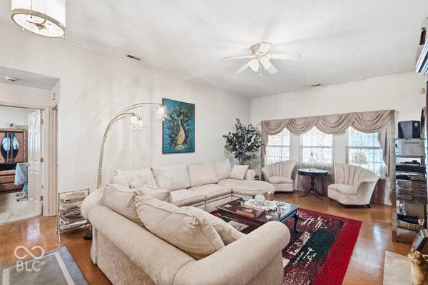 Spacious living area featuring light wood-finish flooring, a contemporary ceiling light fixture, a ceiling fan, and multiple windows with valance treatments