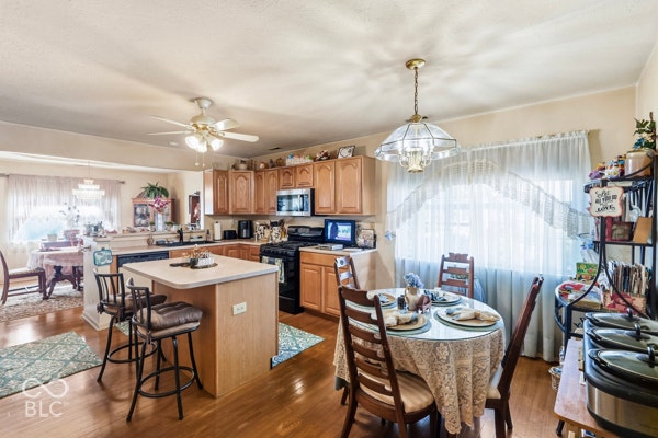 Kitchen featuring wood-finish flooring, light wood cabinetry, a central island with bar seating, and a ceiling fan