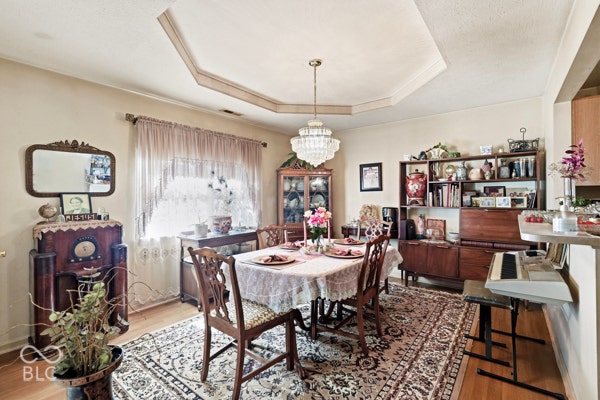 Tray ceiling with crown molding, chandelier lighting, hardwood flooring, and a built-in shelving unit