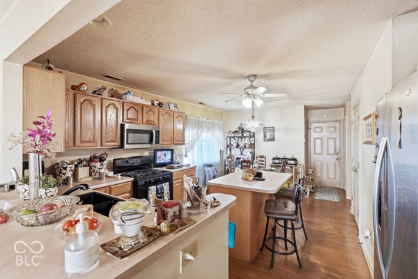 Wood-finish flooring, central island with seating, stainless steel appliances, and wood cabinetry