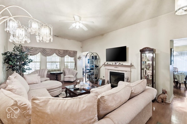 Vaulted ceiling with an attached ceiling fan, recessed fireplace with a stone surround, and wood-finish flooring