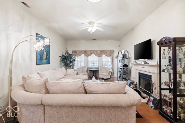 Vaulted ceiling with a ceiling fan, fireplace with a mantel, and wood-finish flooring