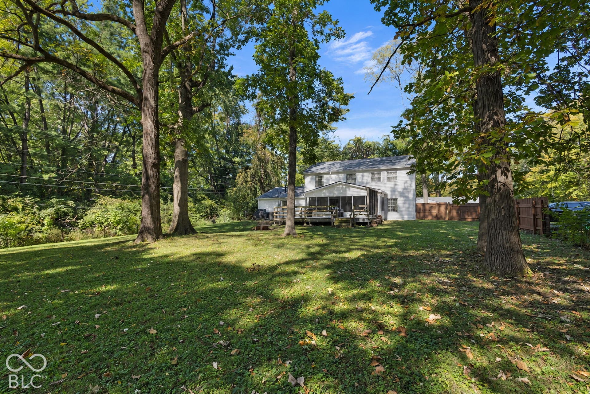 Expansive lawn area with mature trees, featuring a screened porch and an open deck